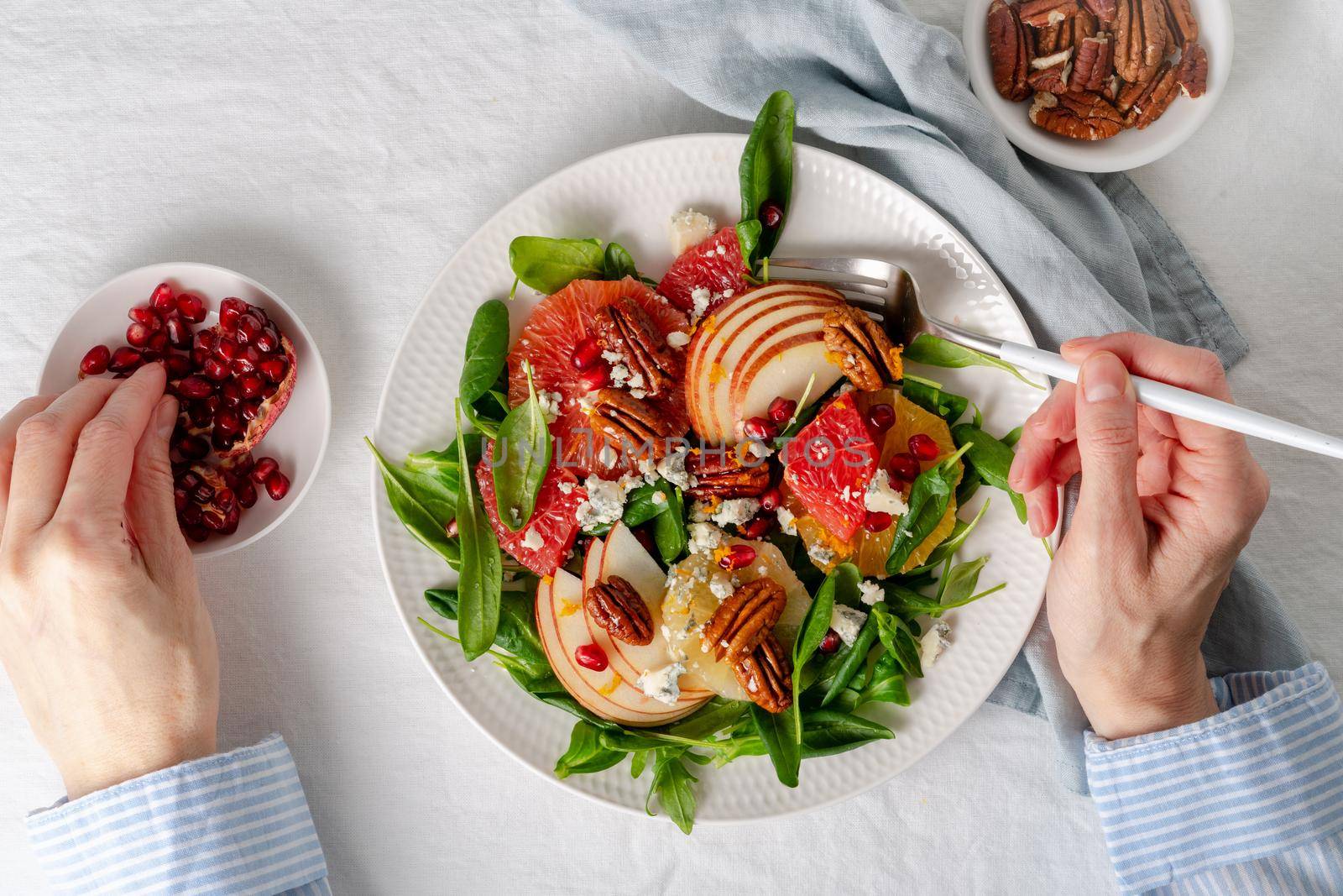 Woman eating Fruits citrus salad with nuts, green lettuce leaves. Balanced food. Top view of hands with plate of meal of Spinach with orange, grapefruit, apples, pecans