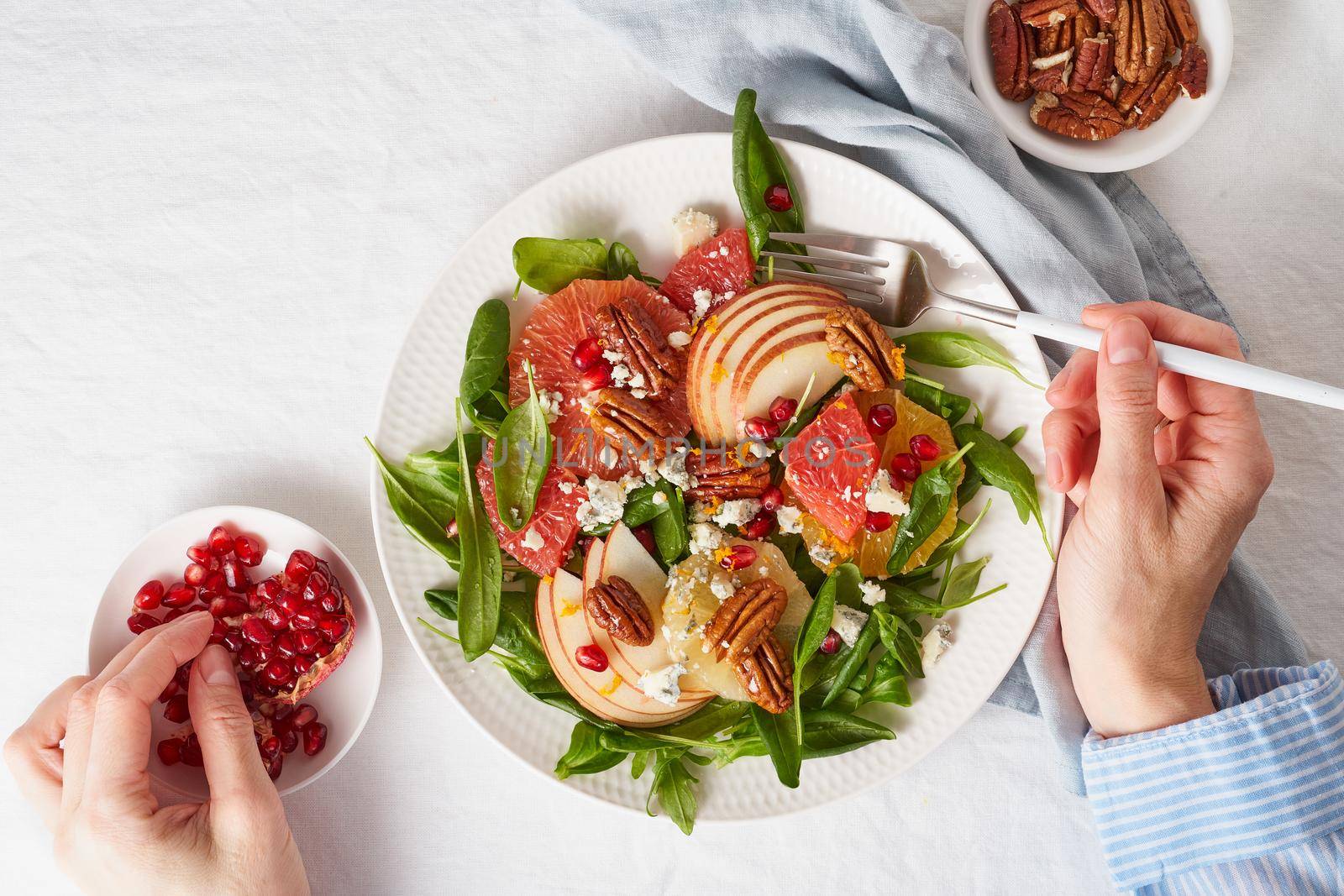 Woman eating Fruits citrus salad with nuts, green lettuce leaves. Balanced food. Top view of hands with plate of meal of Spinach with orange, grapefruit, apples, pecans