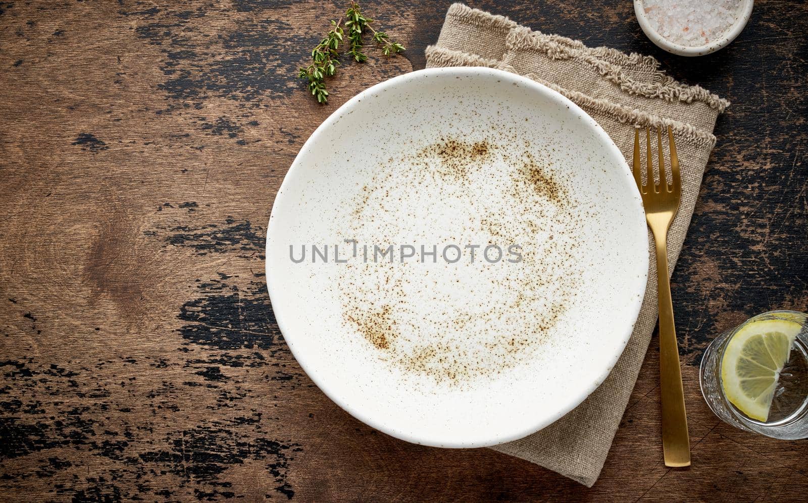 Clean empty white ceramic plate, fork and knife on brown dark old table, copy space, mock up by NataBene