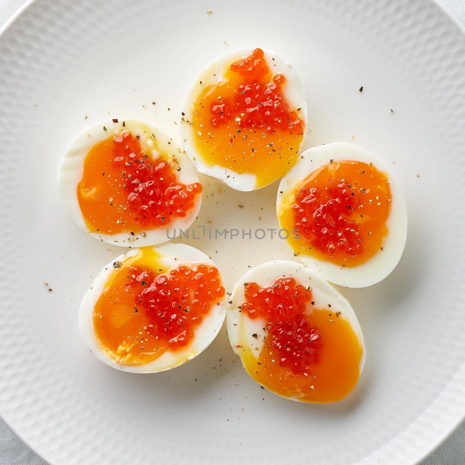 Macro close up of soft-boiled eggs, peeled and cut into two halves, and salmon caviar lying on white plate. High cholesterol, healthy Breakfast, protein food