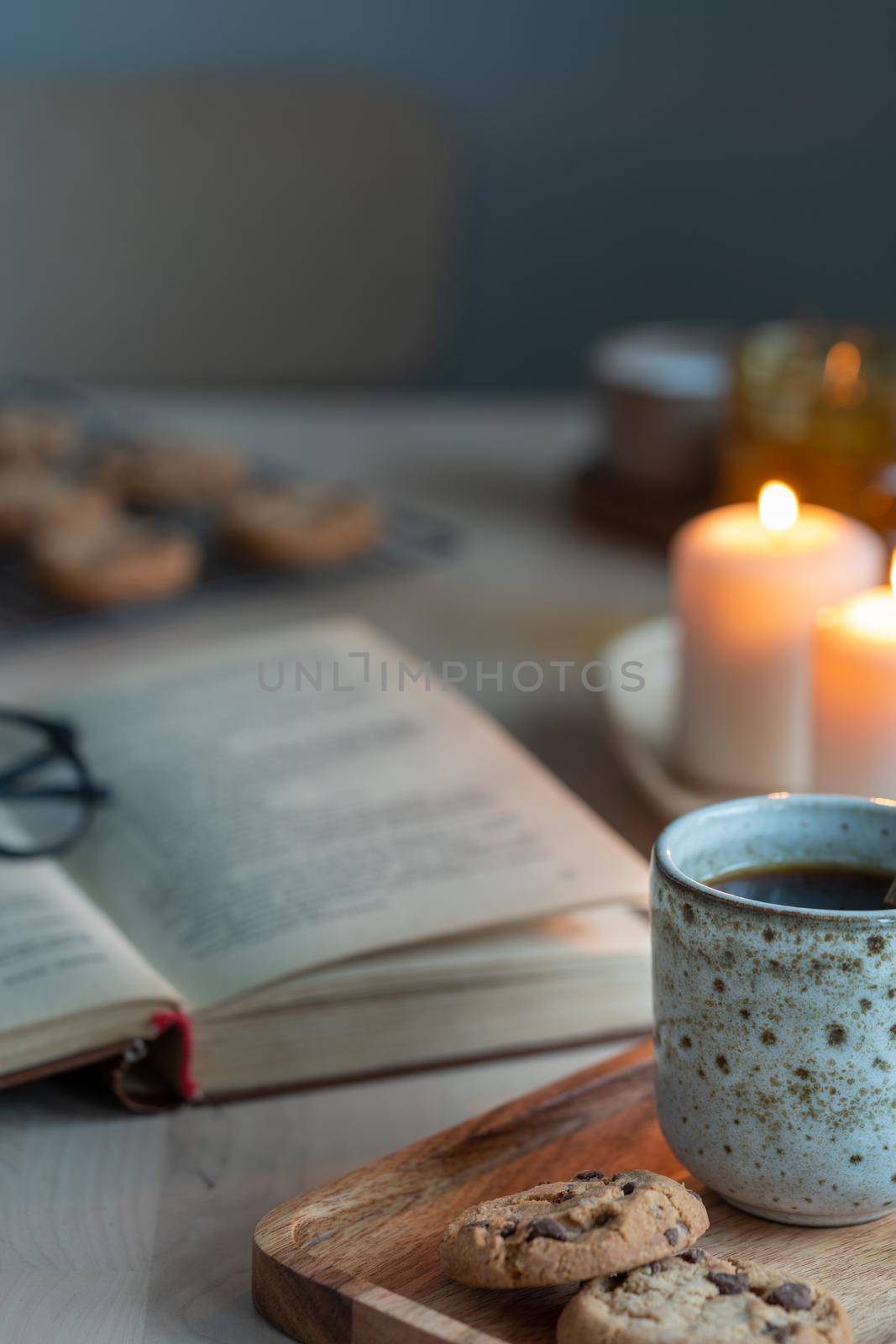 Reading book on cozy winter evening with candles, tea and cookies. Side view, vertical