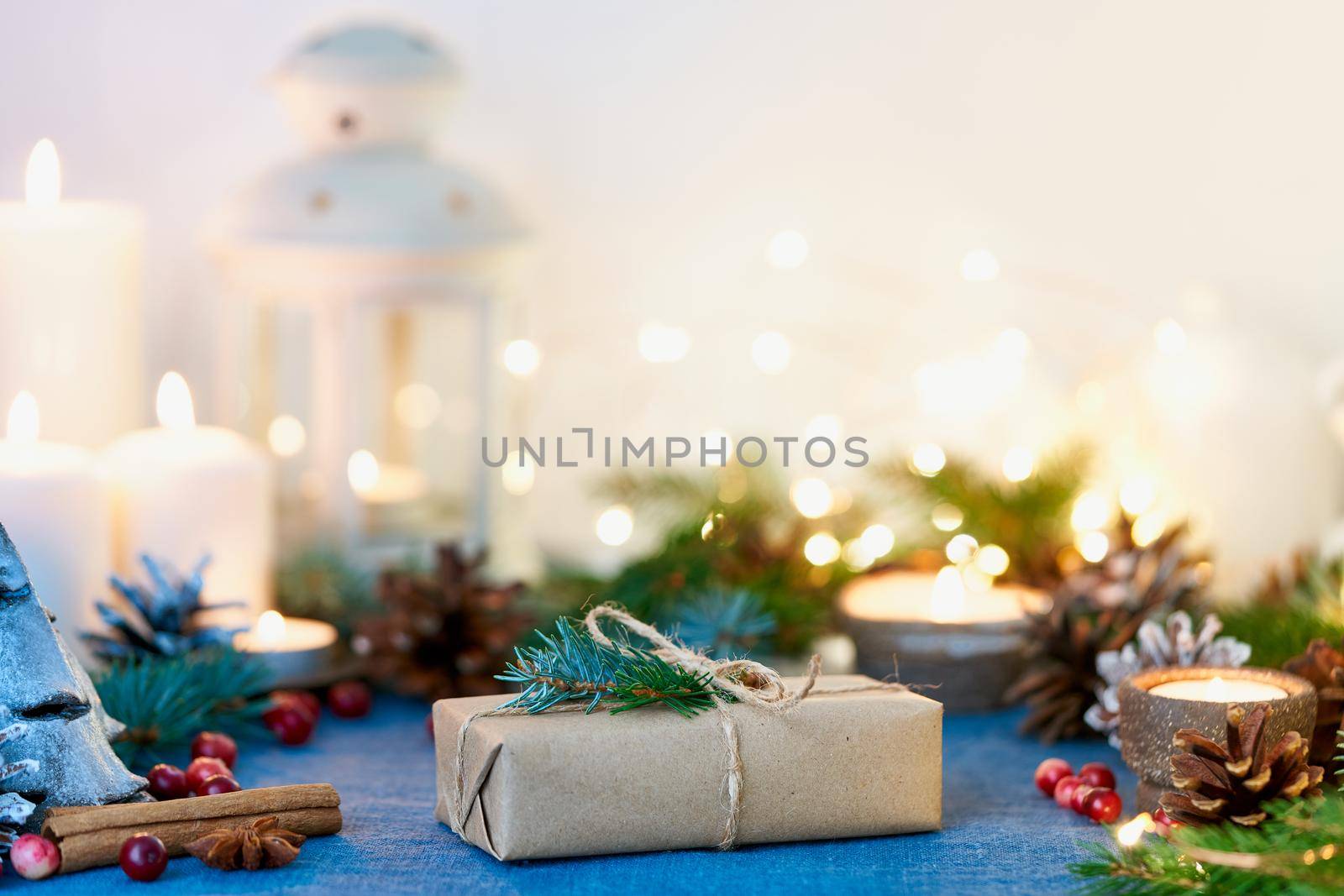 Christmas Background with gift box and decorations, candles and lights garlands. Cozy Happy New Year zero waste white backdrop. Handmade present, fir branches, craft paper , side view