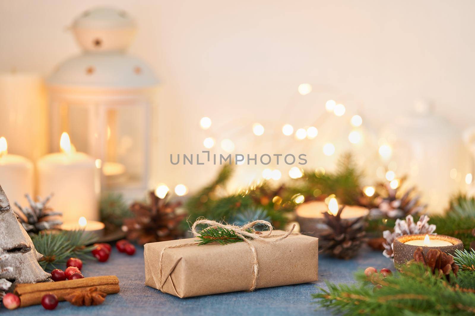 Christmas Background with gift box and decorations, candles and lights garlands. Cozy Happy New Year zero waste white backdrop. Handmade present, fir branches, craft paper , side view