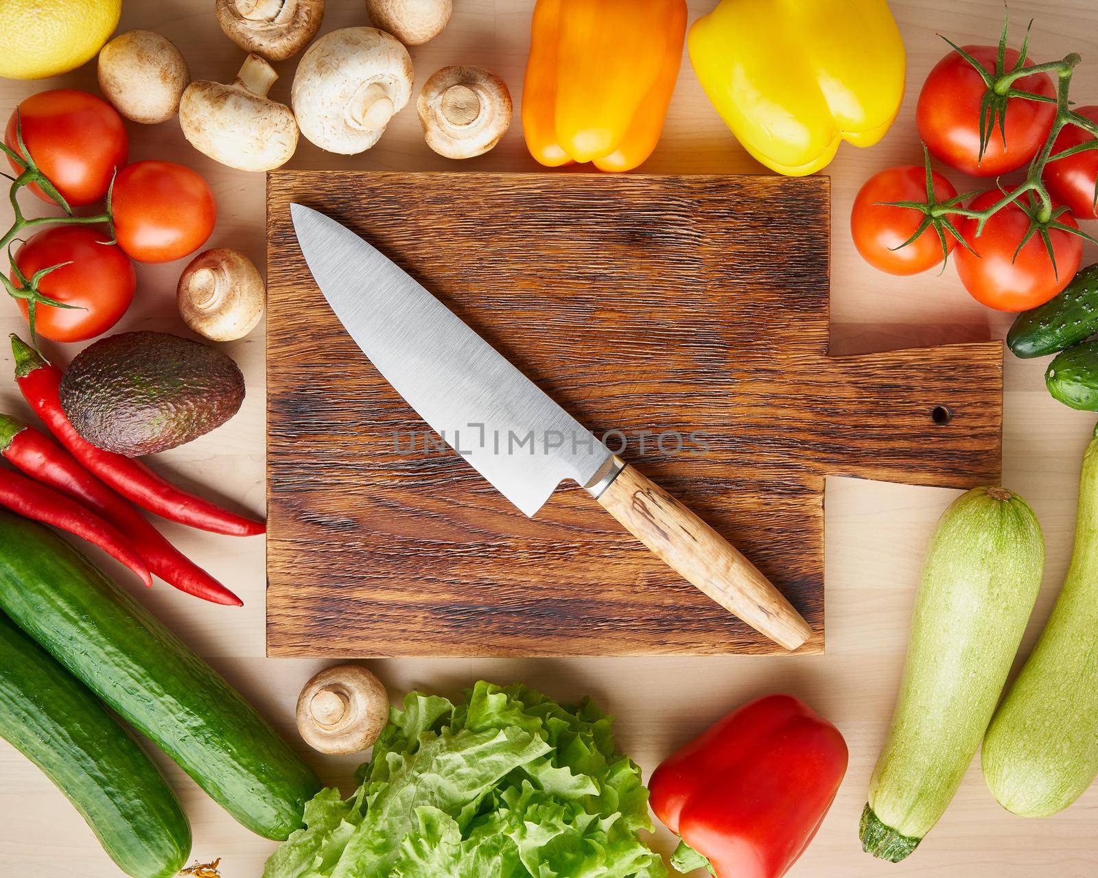 Vegetables around wooden cutting board with knife on kitchen table. Top view. Food ingredient background.