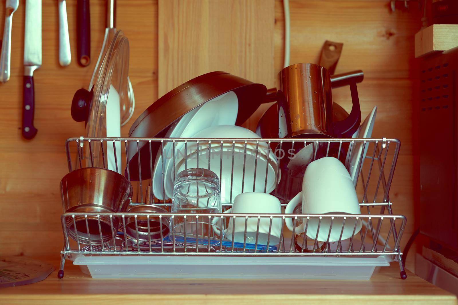 Clean washed dishes are laid out on dryer against background of a wooden wall of country house after breakfast