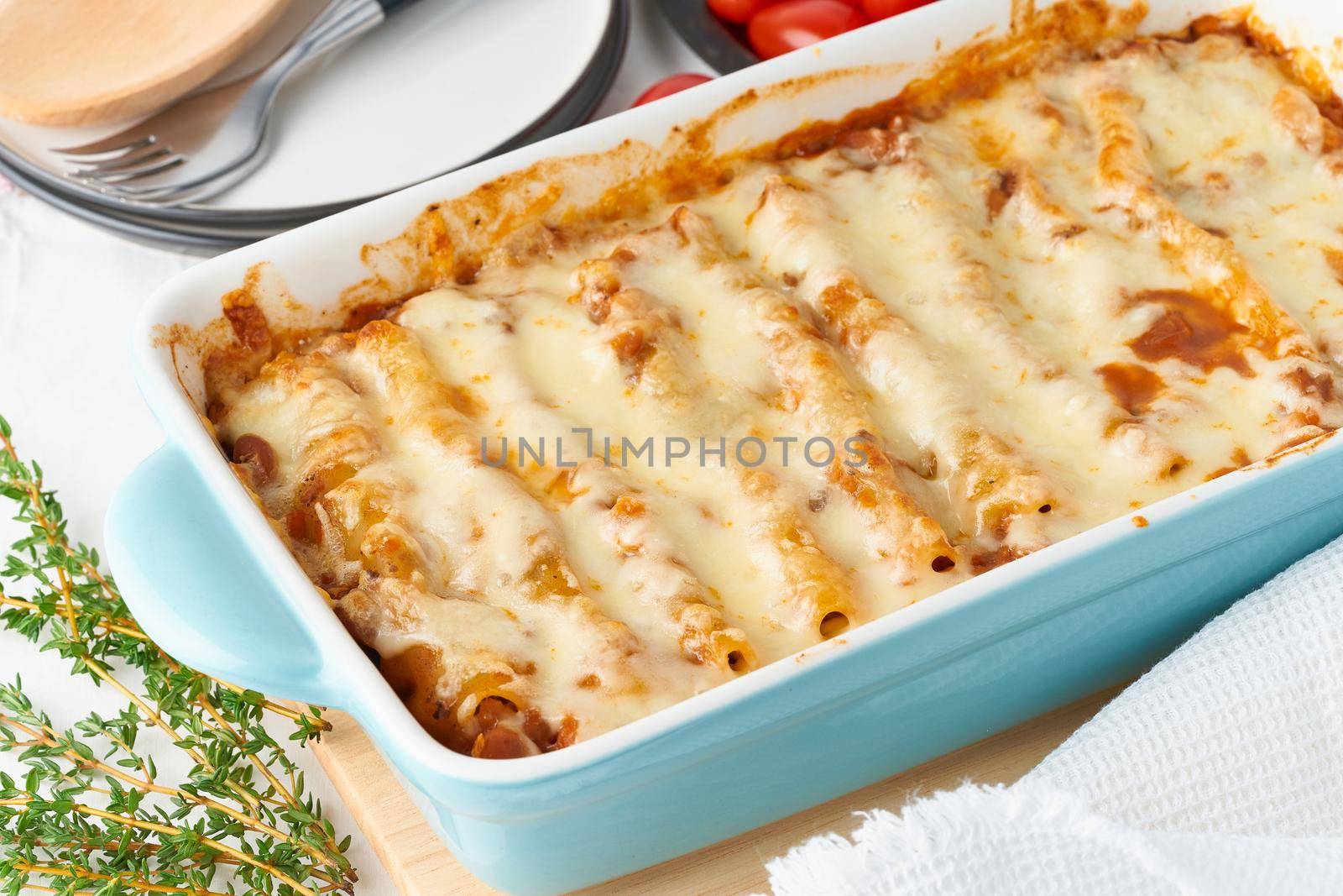 Cannelloni pasta with filling of ground beef, tomatoes, baked with bechamel tomato sauce and a mozzarella. Classical Italian cuisine, white tablecloth with embroidery, rustic style, side view