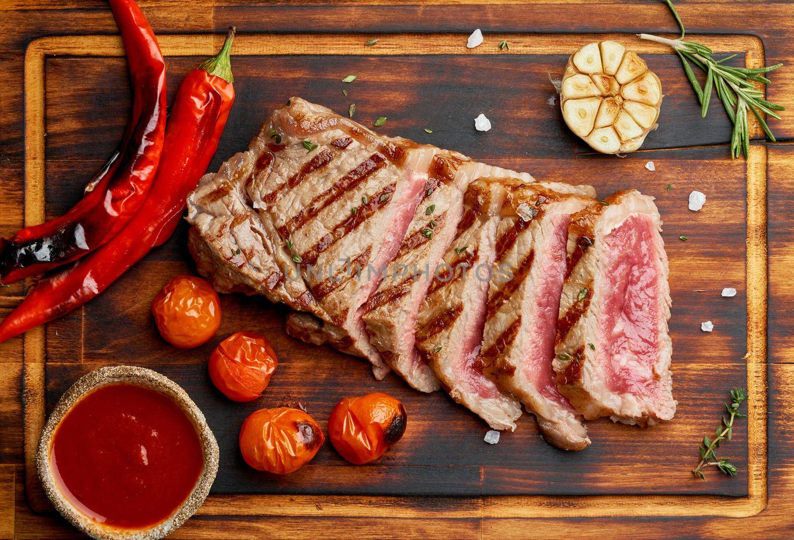 Keto ketogenic diet grilled fried beef steak, striploin on cutting board on dark brown table. Paleo food recipe with grilled fried chopped piece of meat, papper, top view, close up