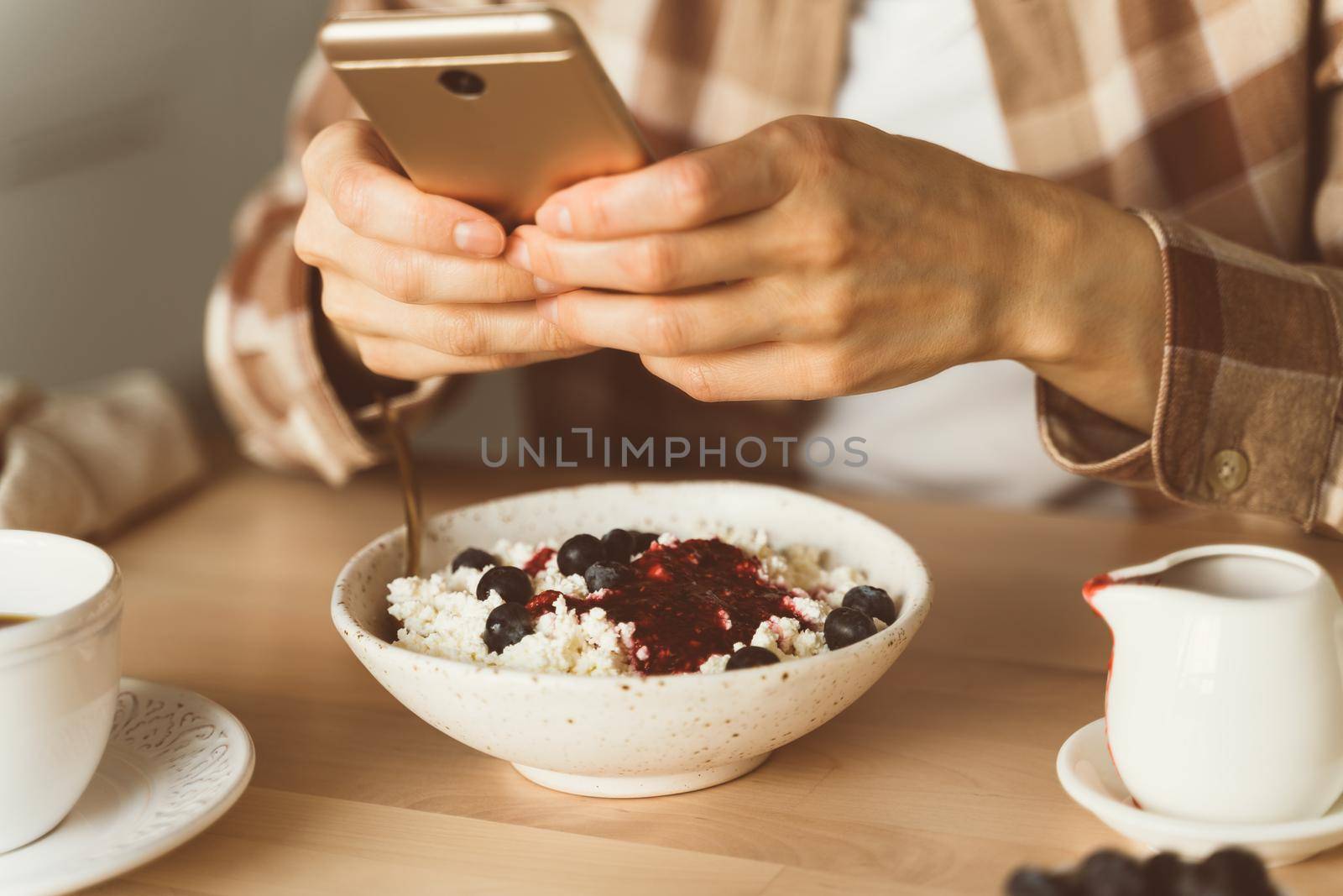 Woman is looking for information on Internet, using mobile, during eating breakfast. Concept for digital addiction. Blogger taking photos of food, shooting Breakfast