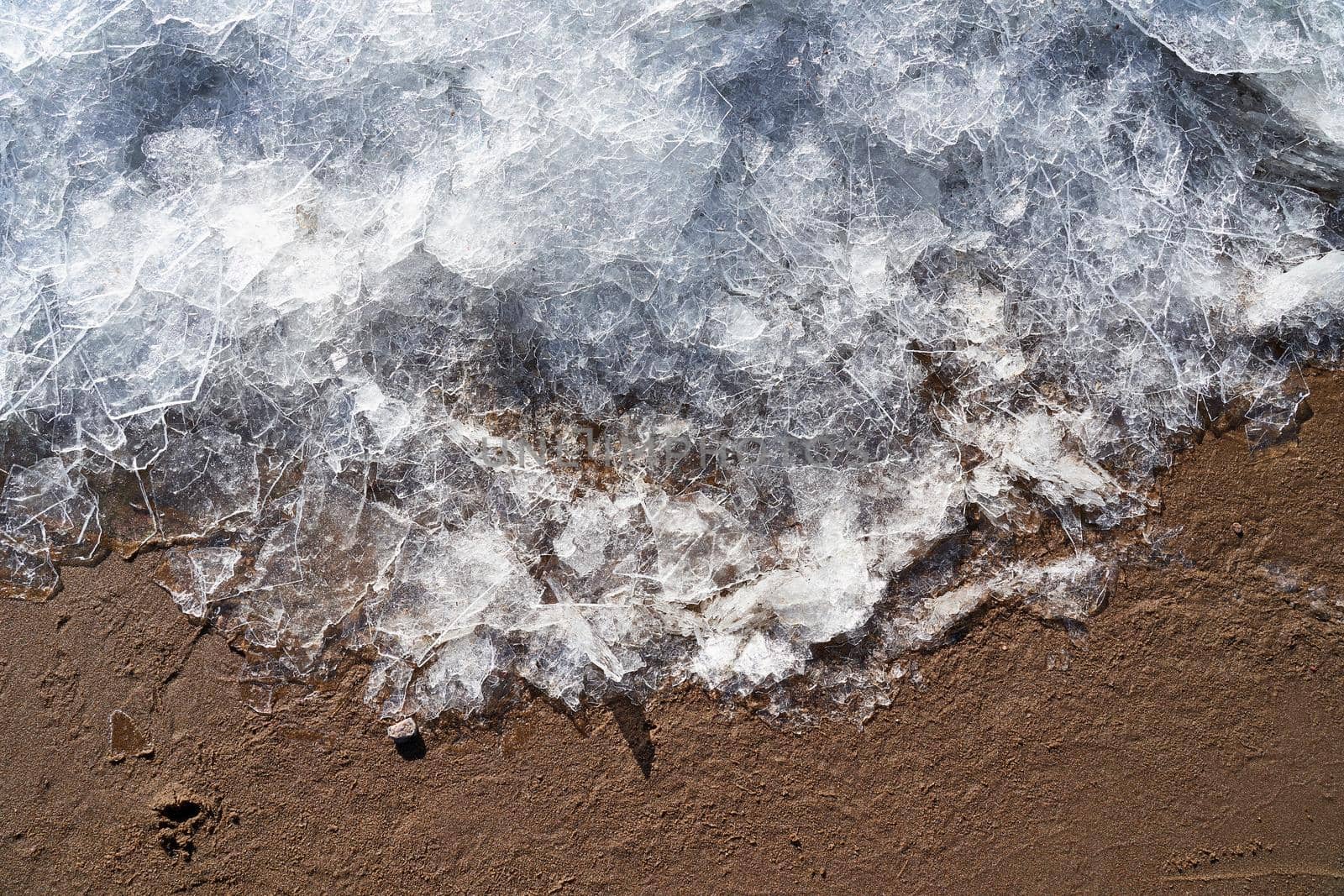Ice on beach. Border of winter and summer. Ice and sand. Cold and warm. Contrast transition of seasons and weather, section