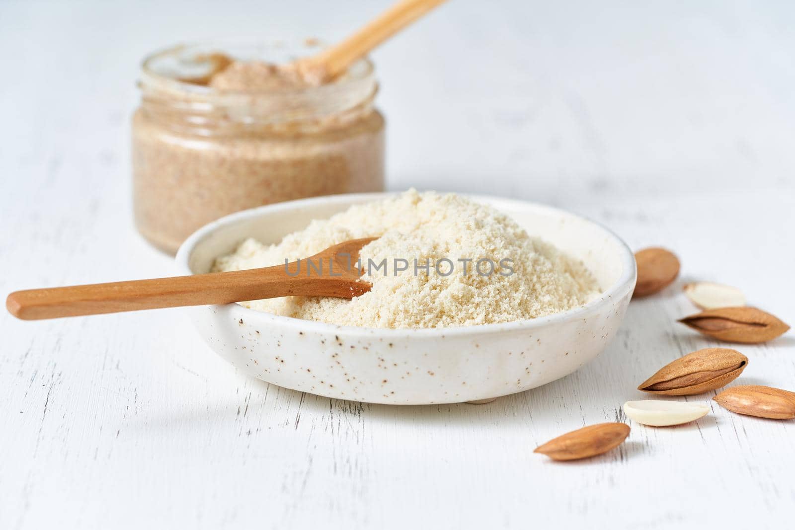 Alternative almond flour. Grated crushed almonds, chopped in a blender, plate, spoon, nuts on the table. White background, side view, close up