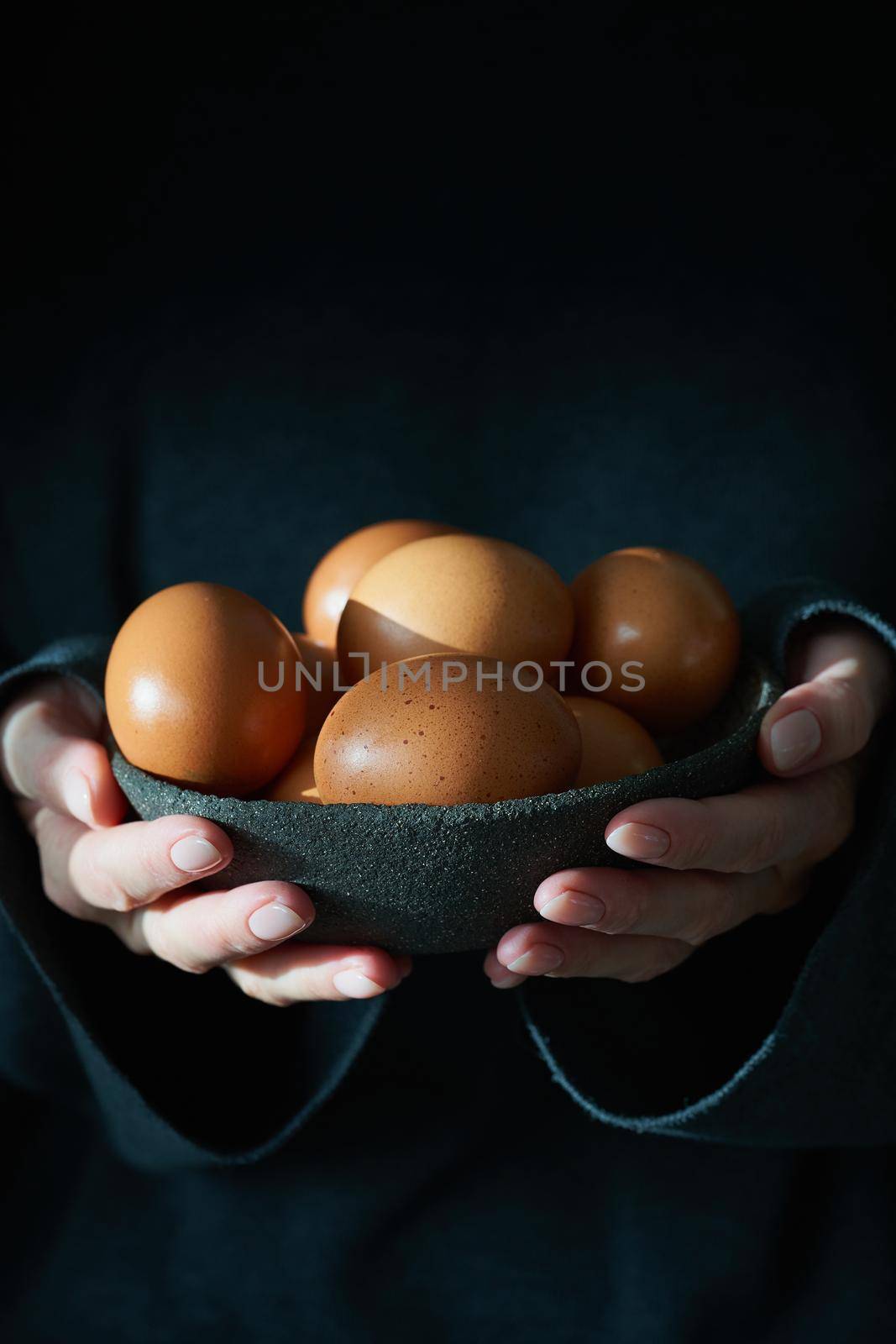 Unusual Easter on dark background. Bowl of brown eggs with hands, vertical by NataBene