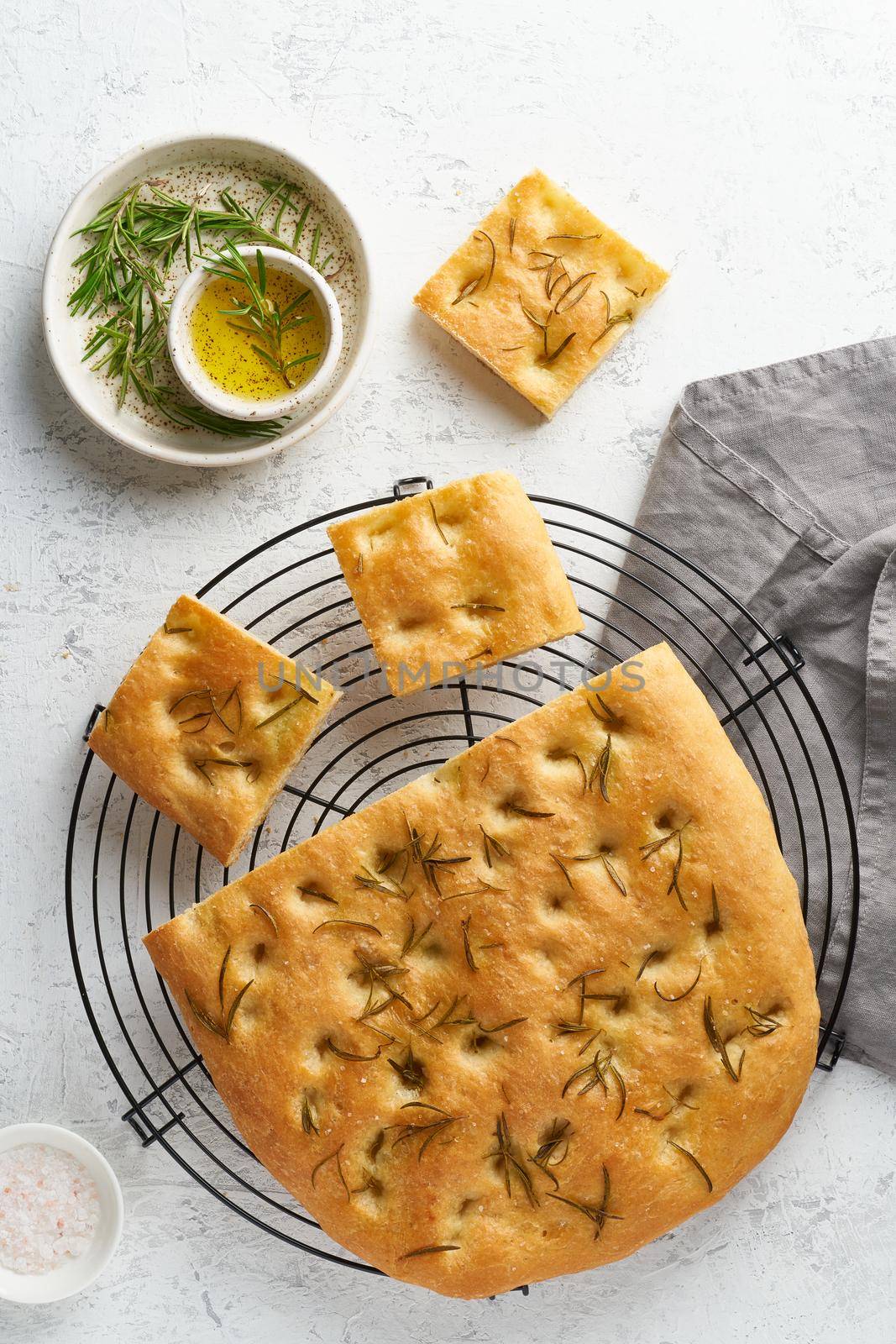 Focaccia, pizza, italian flat bread with rosemary and olive oil on grid on white rustic table, tradition italian cuisine, top view, vertical