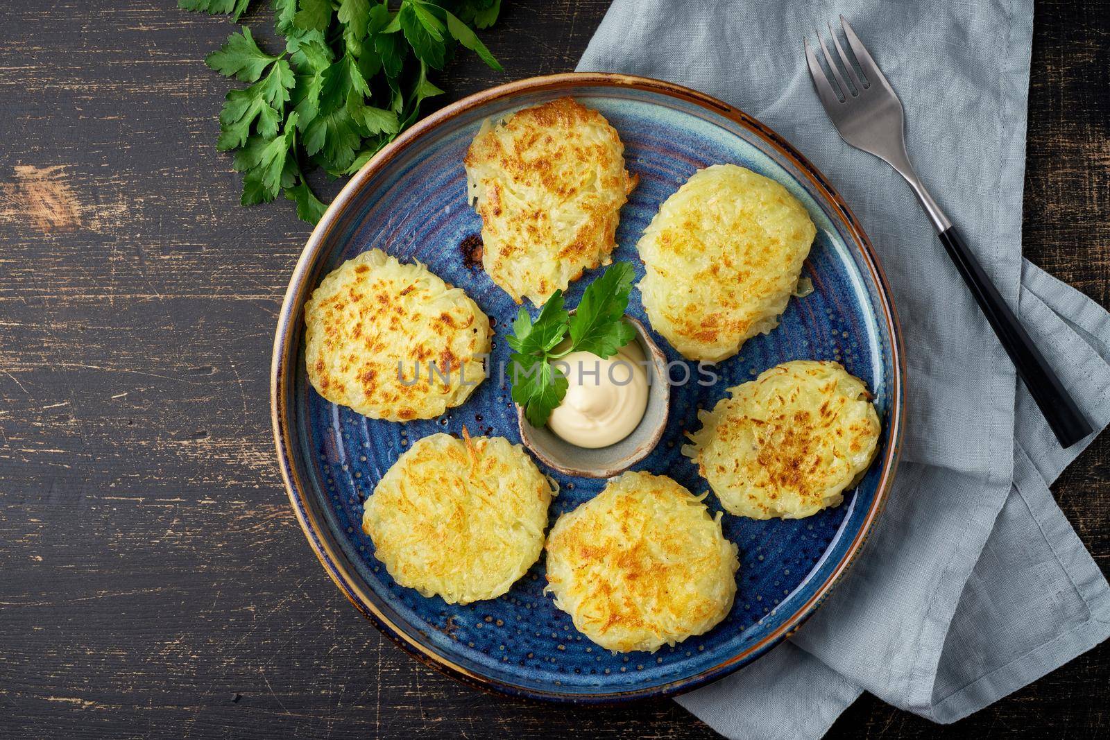 Hashbrown, hash brown potatoes fried pancakes, traditional american cuisine. Crispy hashed browned potatoes in blue plate on dark brown table, top view.