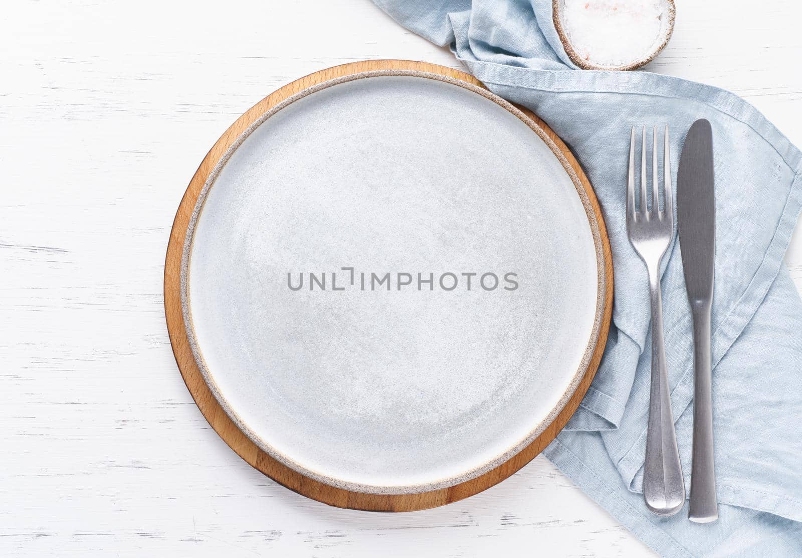 Clean empty white ceramic plate, fork and knife on white stone table, copy space, mock up, top view. Concept for menu with utensil
