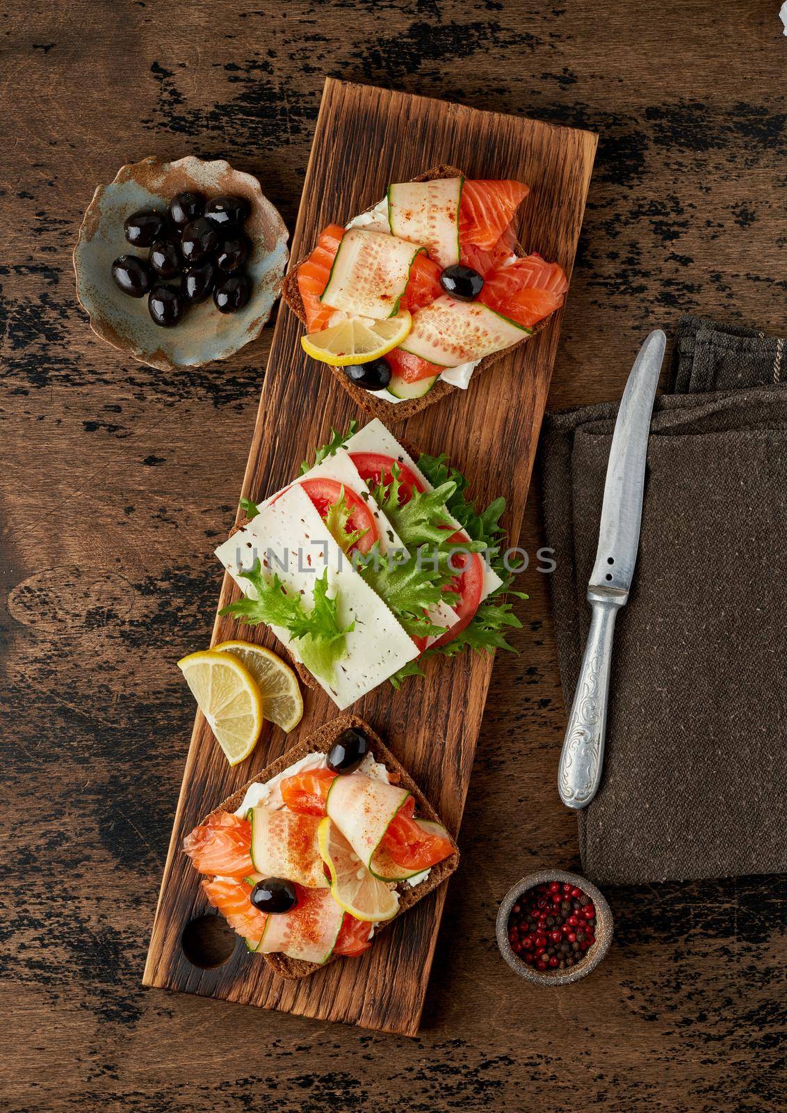 Smorrebrod - traditional Danish sandwiches. Black rye bread with salmon, cream cheese, cucumber, tomatoes on dark brown wooden background, vertical
