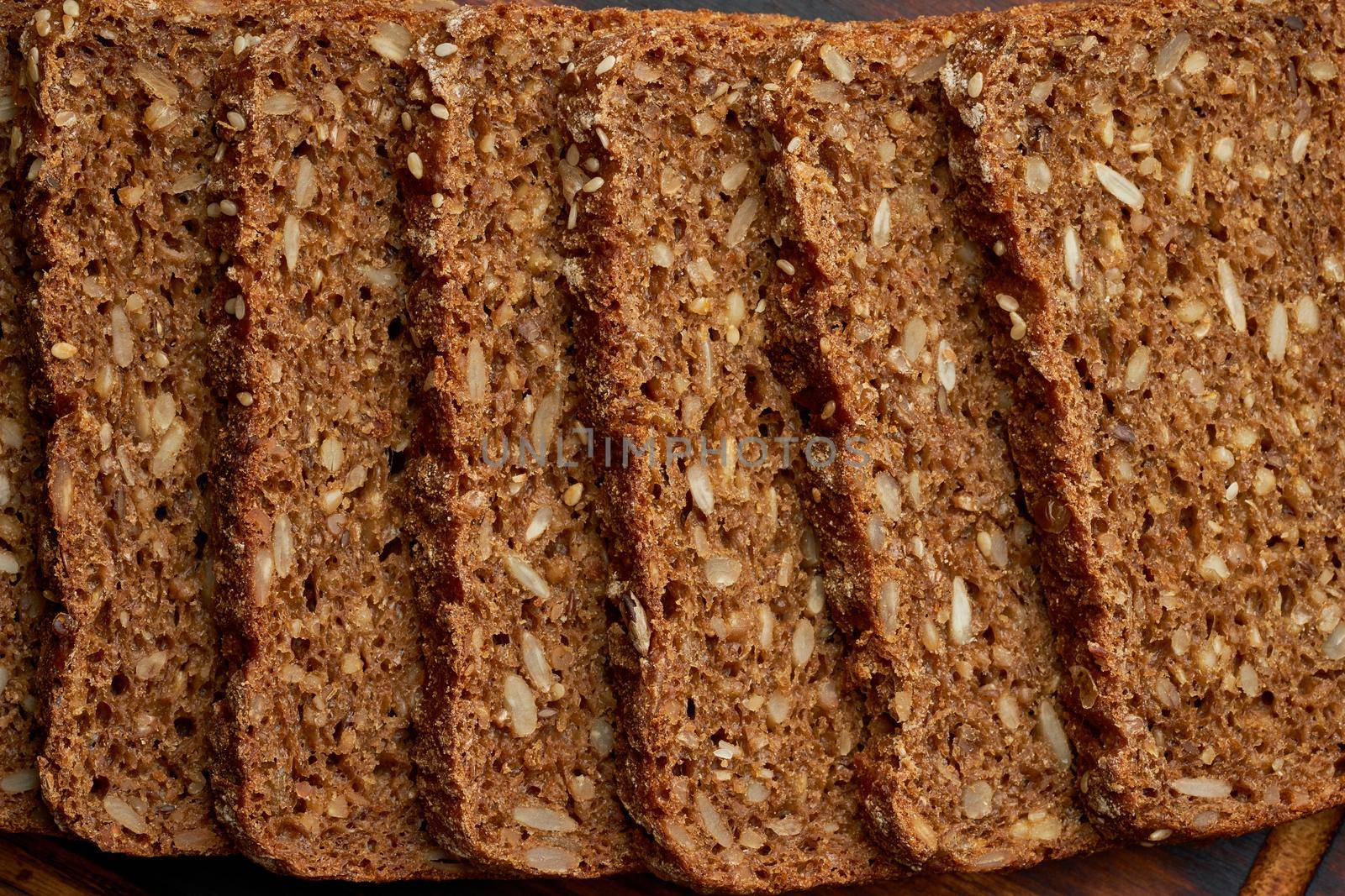Toasted rye grain bread on a wooden cutting board on dark brown background. Slices of flour pastry with lectins, top view, macro, banner
