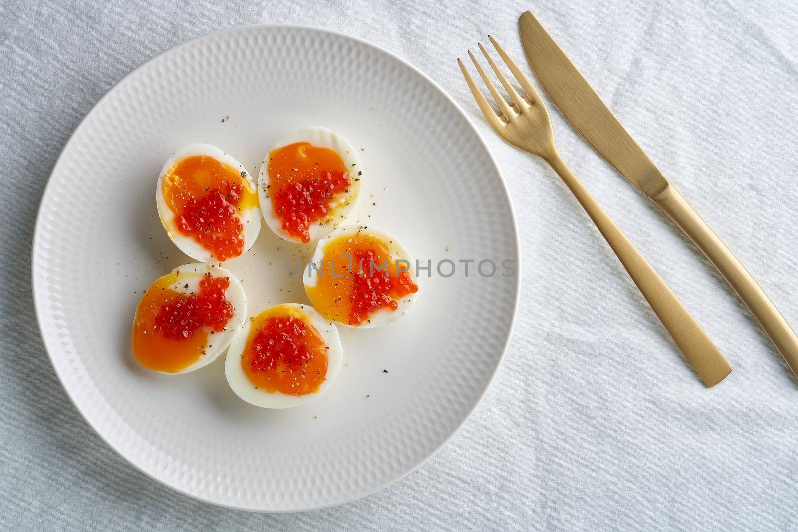 Soft-boiled eggs, peeled and cut into two halves, and salmon caviar lying on white plate. High cholesterol, healthy Breakfast, protein food