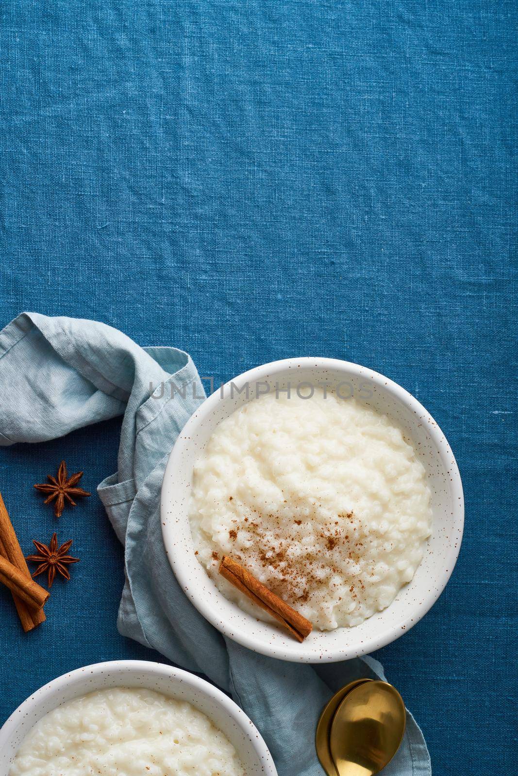 Rice pudding. French milk rice dessert. Healthy Vegan diet breakfast with coconut milk, cinnamon. Blue linen textile. Dark background. Top view, vertical, copy space