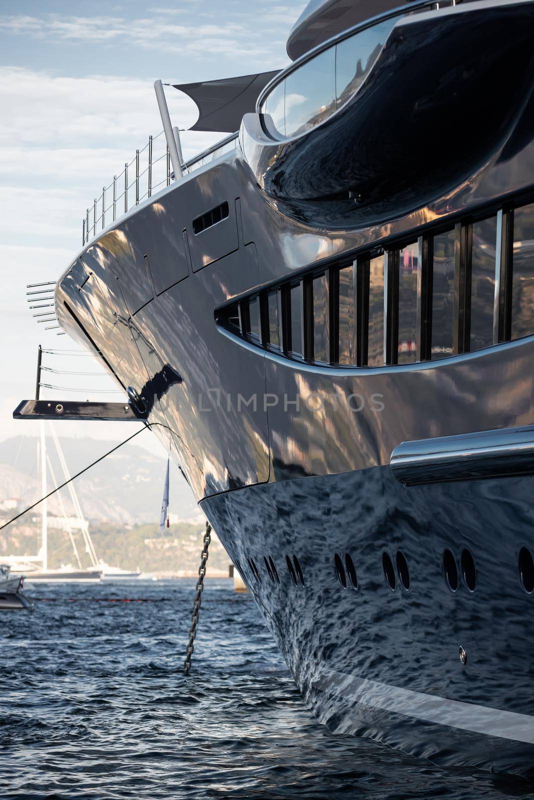 The mesmerizing reflection of the water on the glossy side of a huge yacht anchored, chrome details, chains and ropes to the muring descend into the water. High quality photo