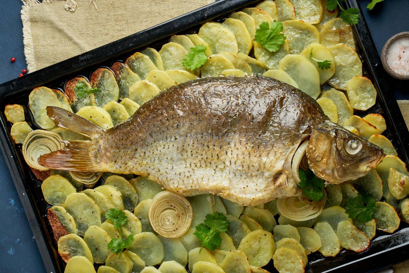 Baked carp, whole fish from the oven with sliced potatoes on a large tray. Traditional European Polish dish, suitable for a Christmas table, top view, close up