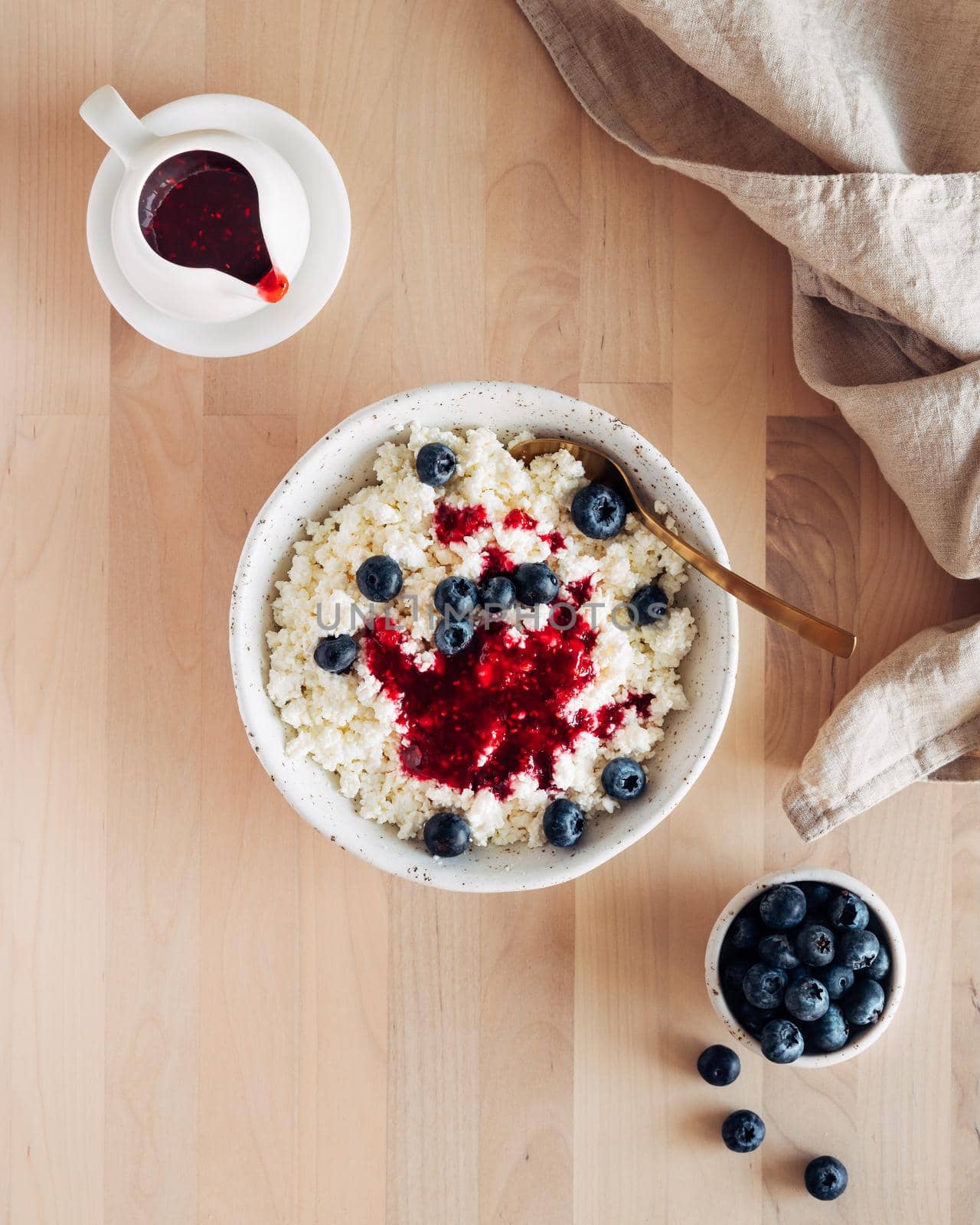 White bowl of homemade curd with jam, raspberries, blueberries on brown wooden table, top view, close up, vertical