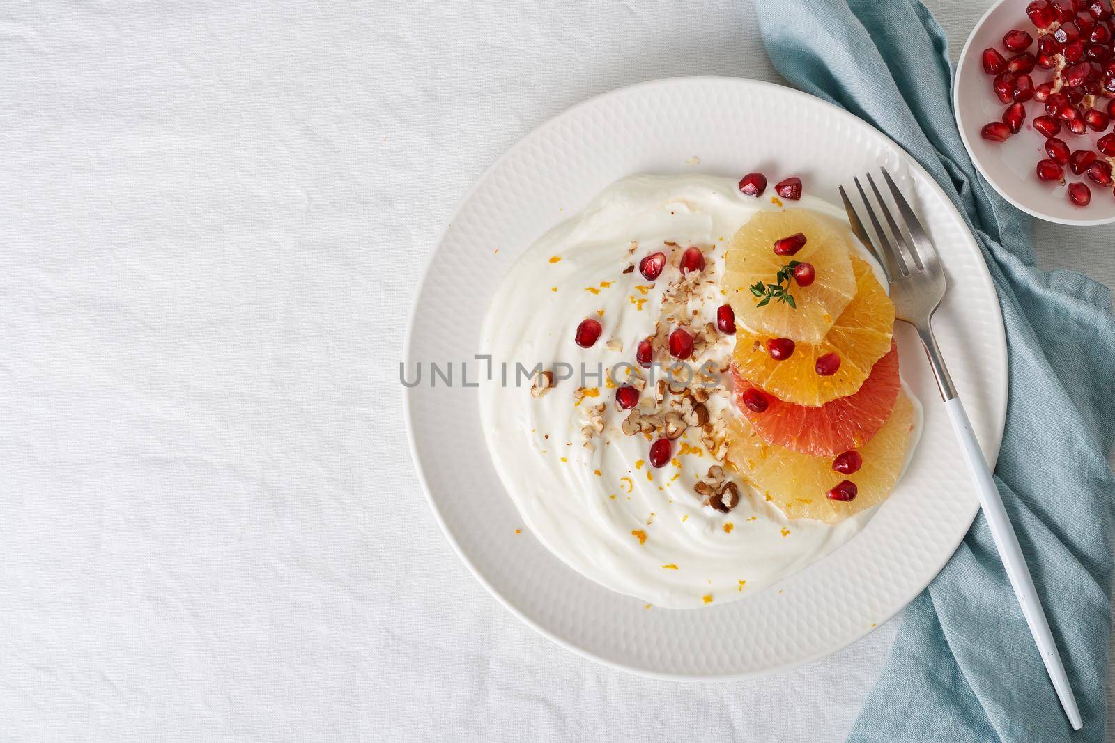 Ricotta with citrus fruits, pecans and honey on white plate on white table. Sweet and healthy colorful dessert, Mixed fruit salad with coconut yoghurt. Copy space, top view