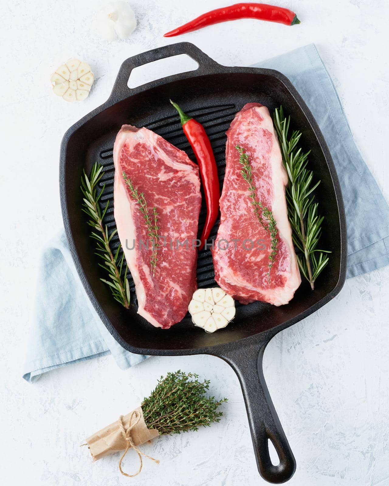 Two fresh raw big whole pieces of meat, beef fillet, marble striploin in cast-iron large pan. Top view, close up, vertical. Seasoning steak with salt.