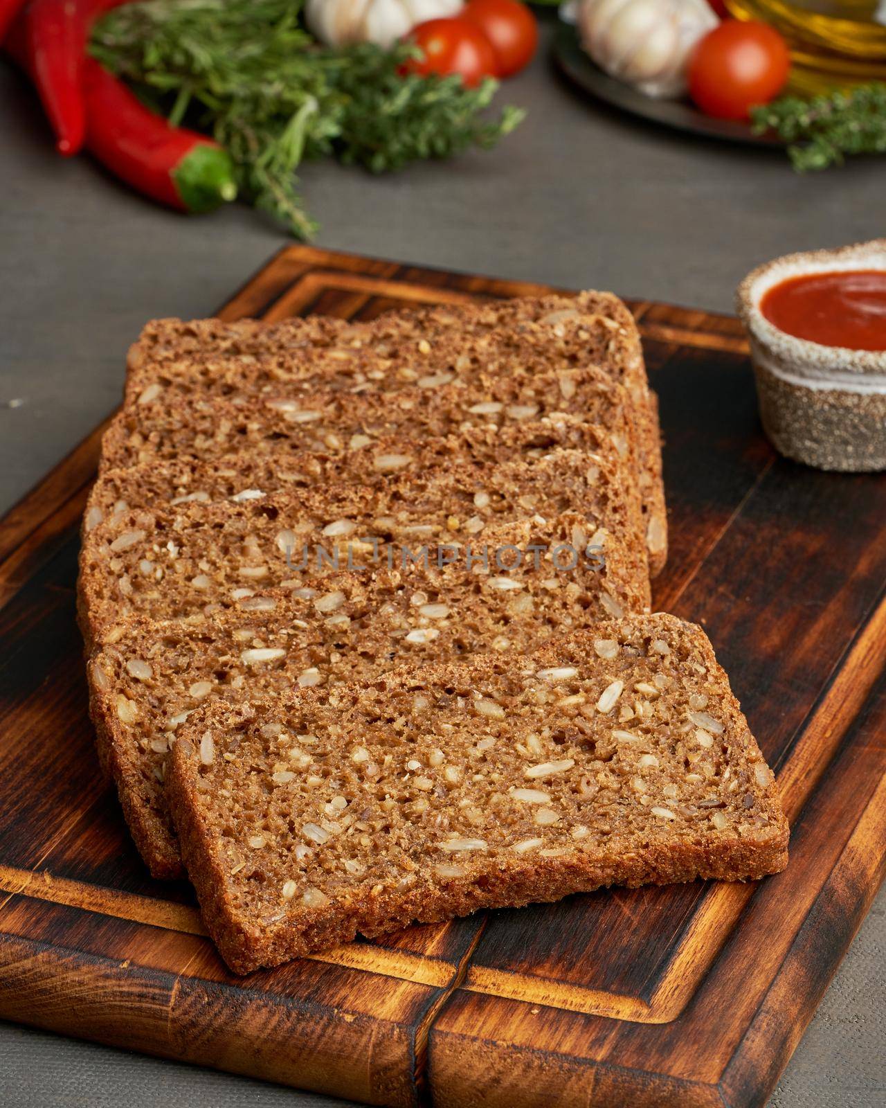 Toasted rye grain bread on a wooden cutting board on dark brown background. Slices of flour pastry with lectins, side view, vertical