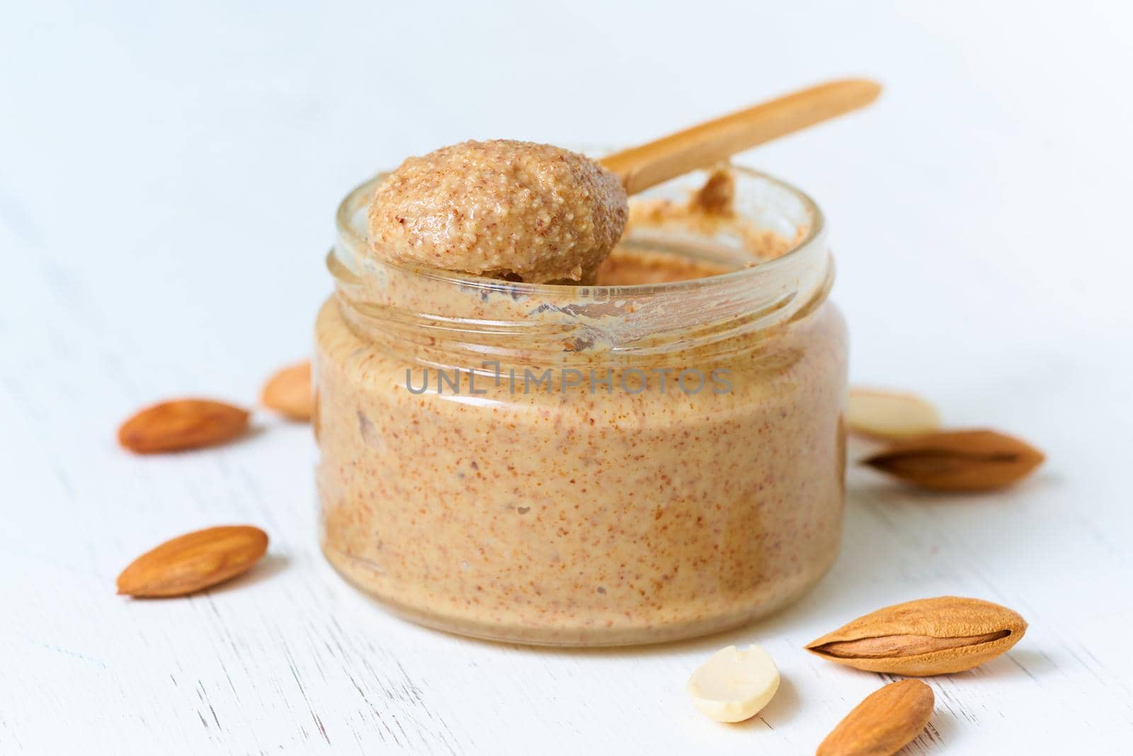 Almond butter, raw food paste made from grinding almonds into nut butter, crunchy and stir, white wooden table, glass jar, side view, close up
