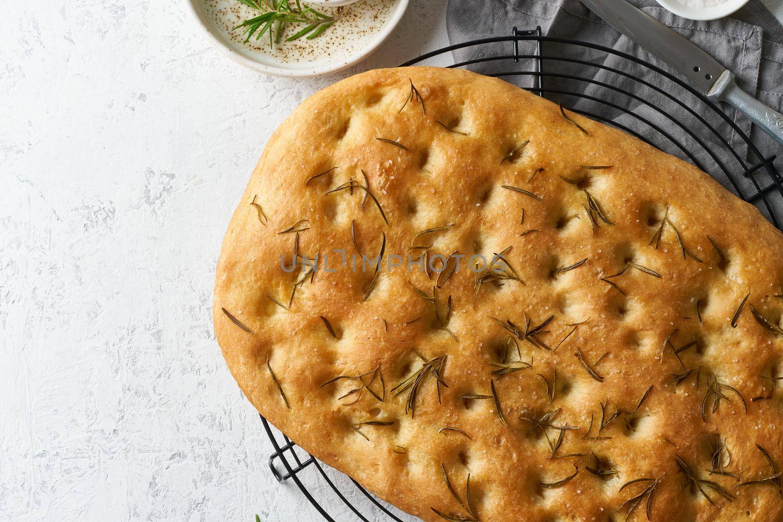 Focaccia, pizza, flat bread with rosemary and olive oil on grid on white rustic table, tradition italian cuisine, top view, copy space