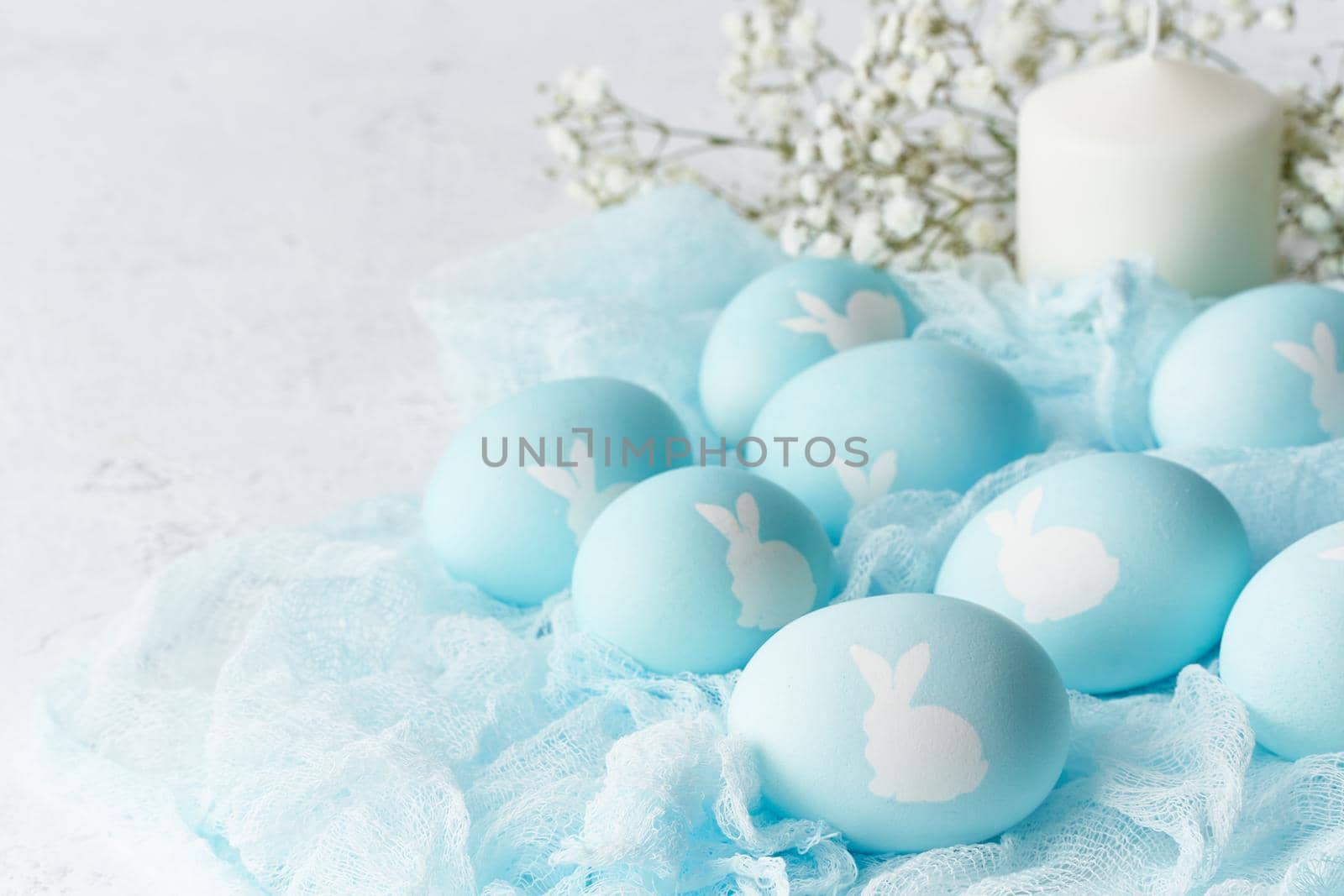 Easter. Holiday. Light white background, gentle pastel colors. Blue eggs with image of rabbit in basket. Flowers in background, side view, copy space