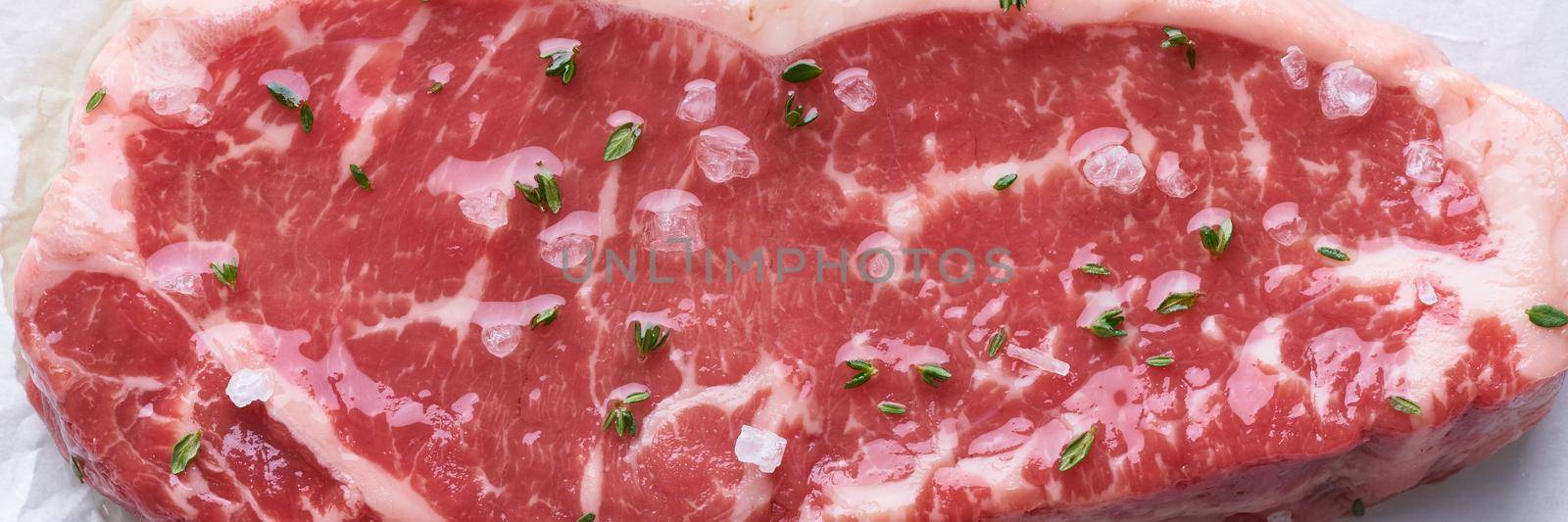 Big whole piece of raw beef meat, striploin. Steak with seasoning and salt. Top view, close up. Long width banner