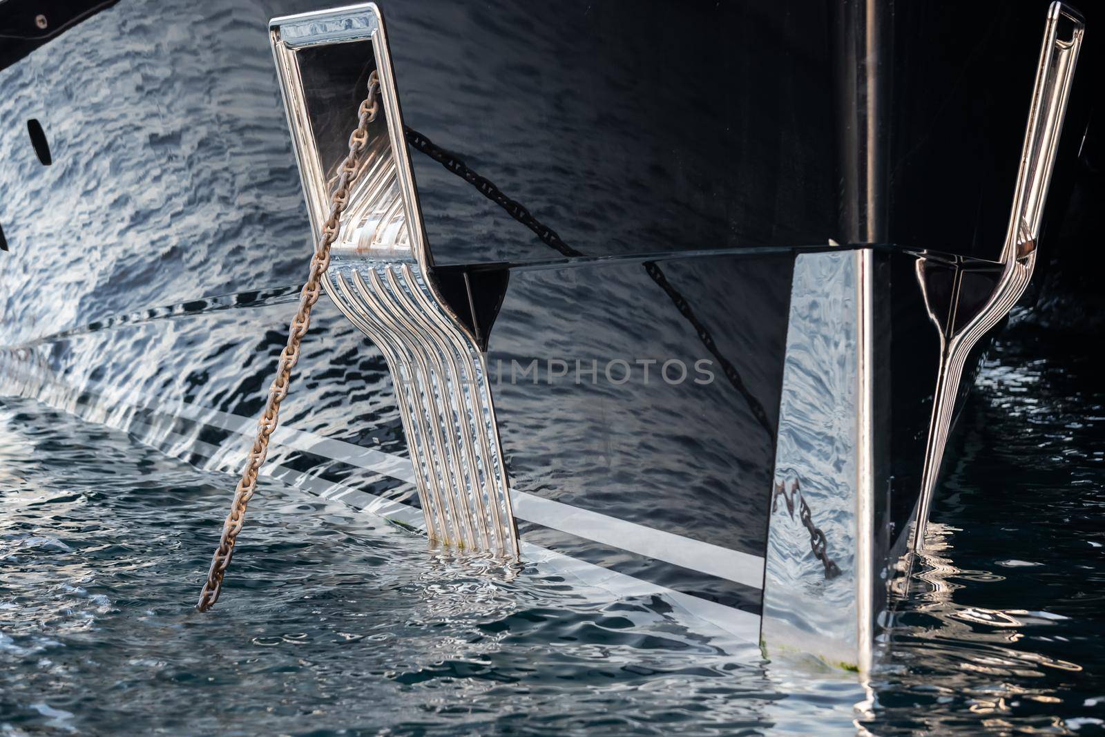 The mesmerizing reflection of the water on the glossy side of a huge yacht anchored, chrome details, chains and ropes to the muring descend into the water. High quality photo