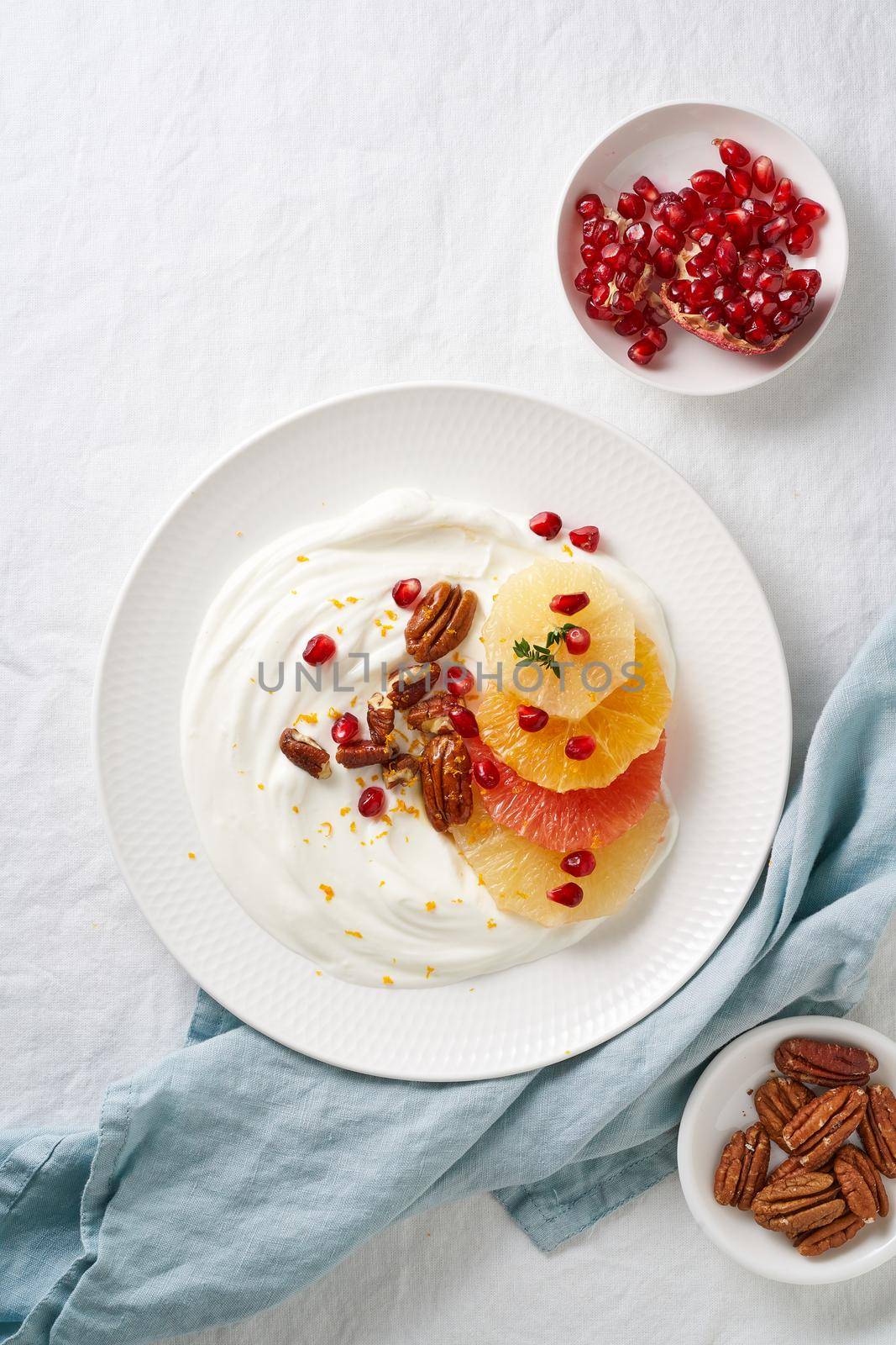 Ricotta with citrus fruits, pecans and honey on white plate on white table. Sweet and healthy colorful dessert with yogurt and pomegranate seeds. Vertical, top view