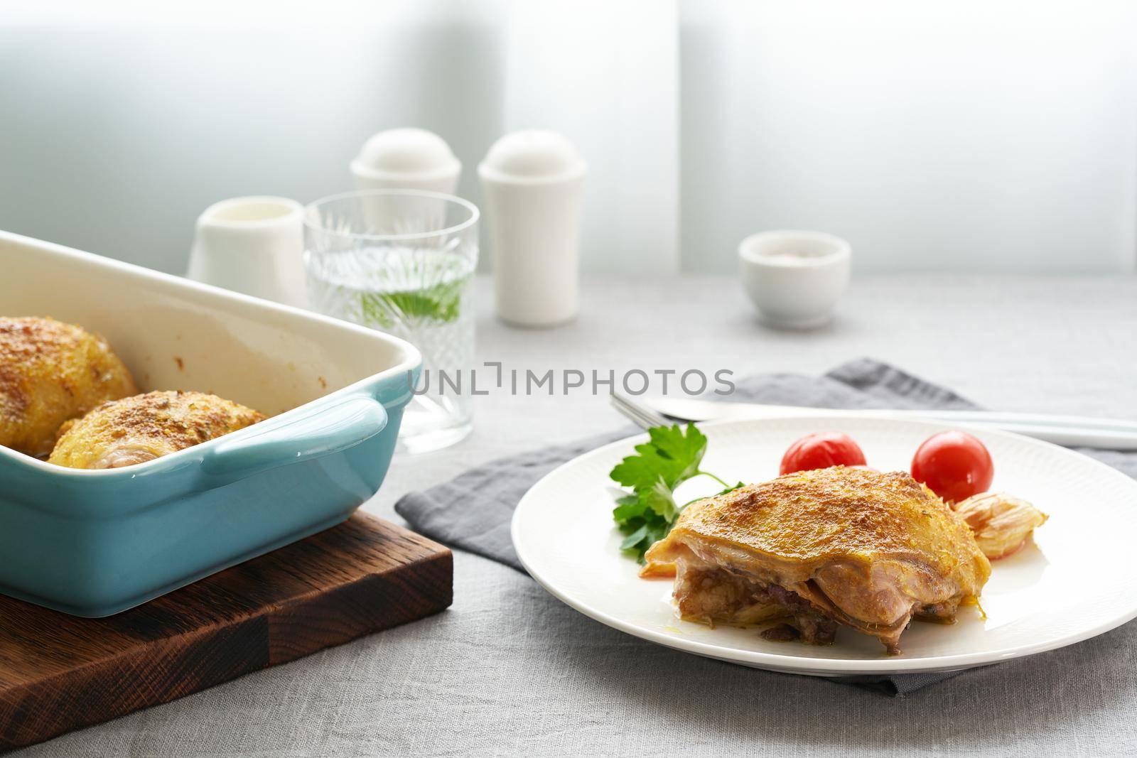 Chicken thighs baked with turmeric, tomatoes and garlic. Fried chicken is on plate, gray tablecloth, tray of meat. Healthy diet, clean eating, paleo, keto, ketogenic