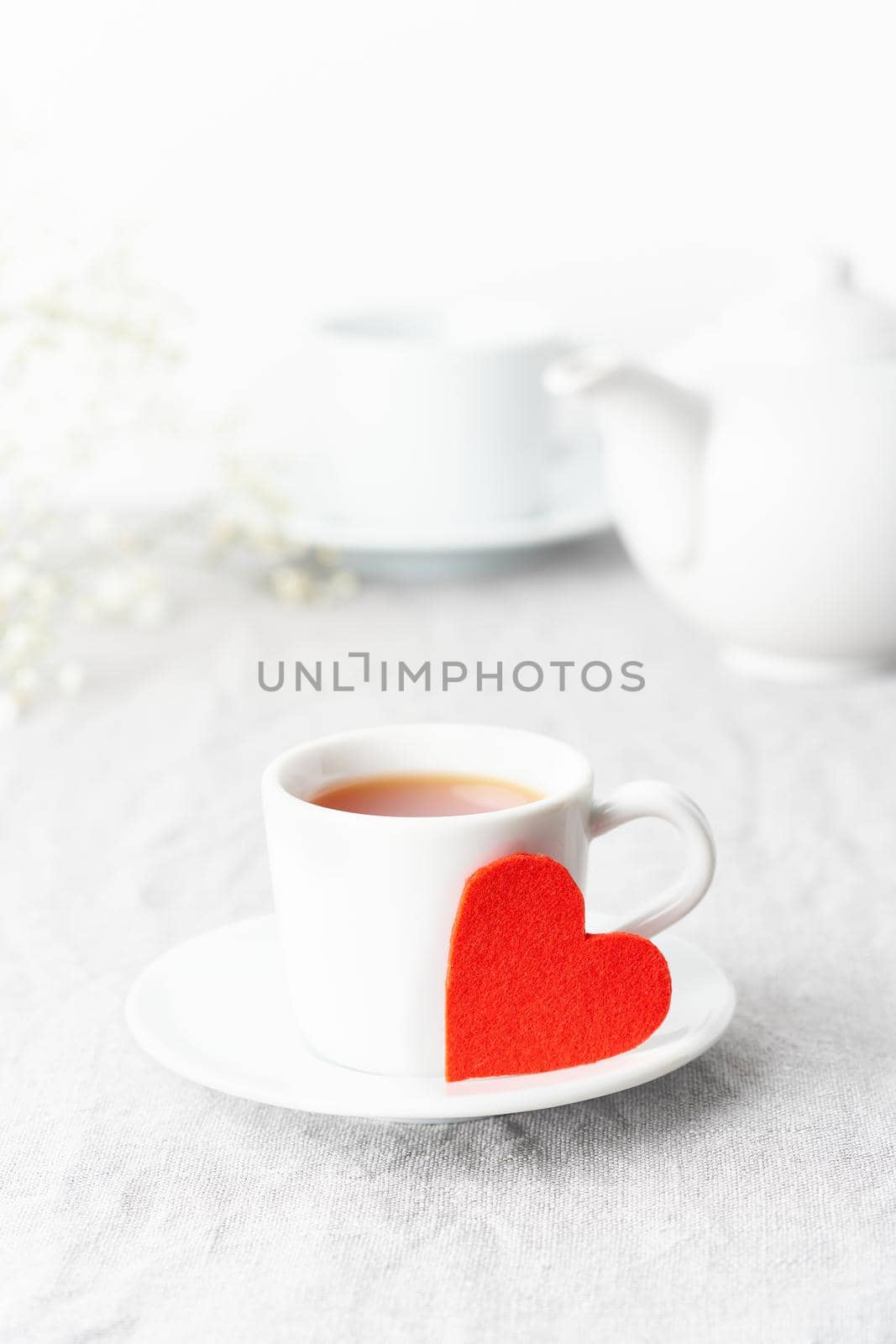 Valentine's Day. Morning breakfast for two with tea and flowers. Red felt heart is symbol of lovers. Light white tender pastel background. Vertical, copy space. Scandinavian minimalism