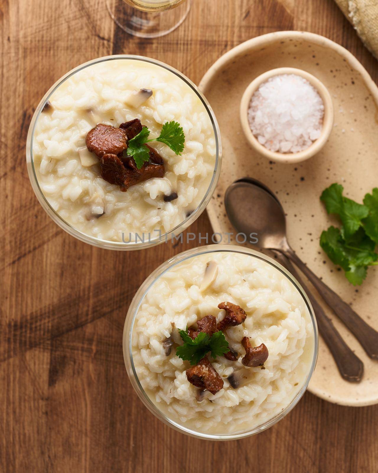 Risotto with mushrooms in wine glass. Unconventional unusual serving. Rice porridge with mushrooms. Wooden old table. Hot dish in glass bowl. Top view, selective focus