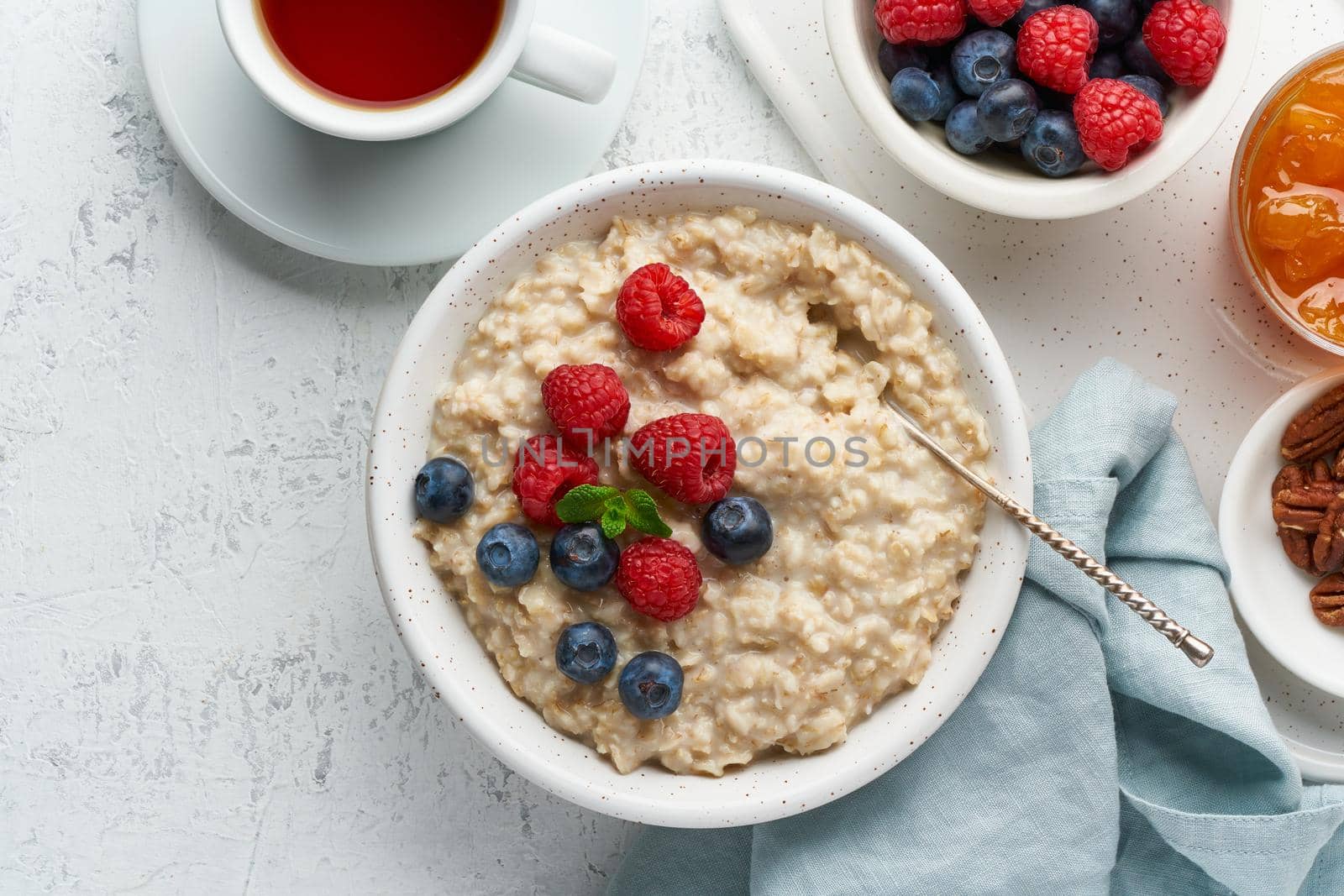 Oatmeal porridge with blueberry, raspberries, jam and nuts in white bowl, dash diet with berries, white background, top view copy space. Healthy diet breakfast