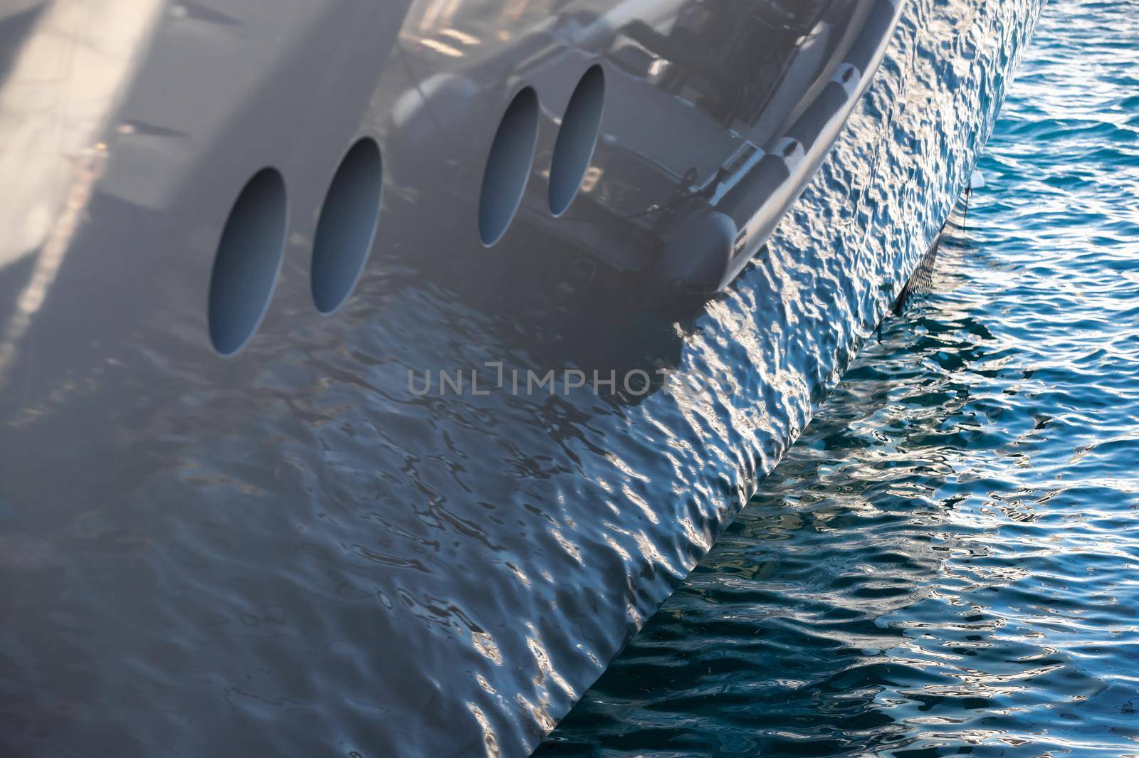 The mesmerizing reflection of the water on the glossy side of a huge yacht anchored, chrome details. High quality photo