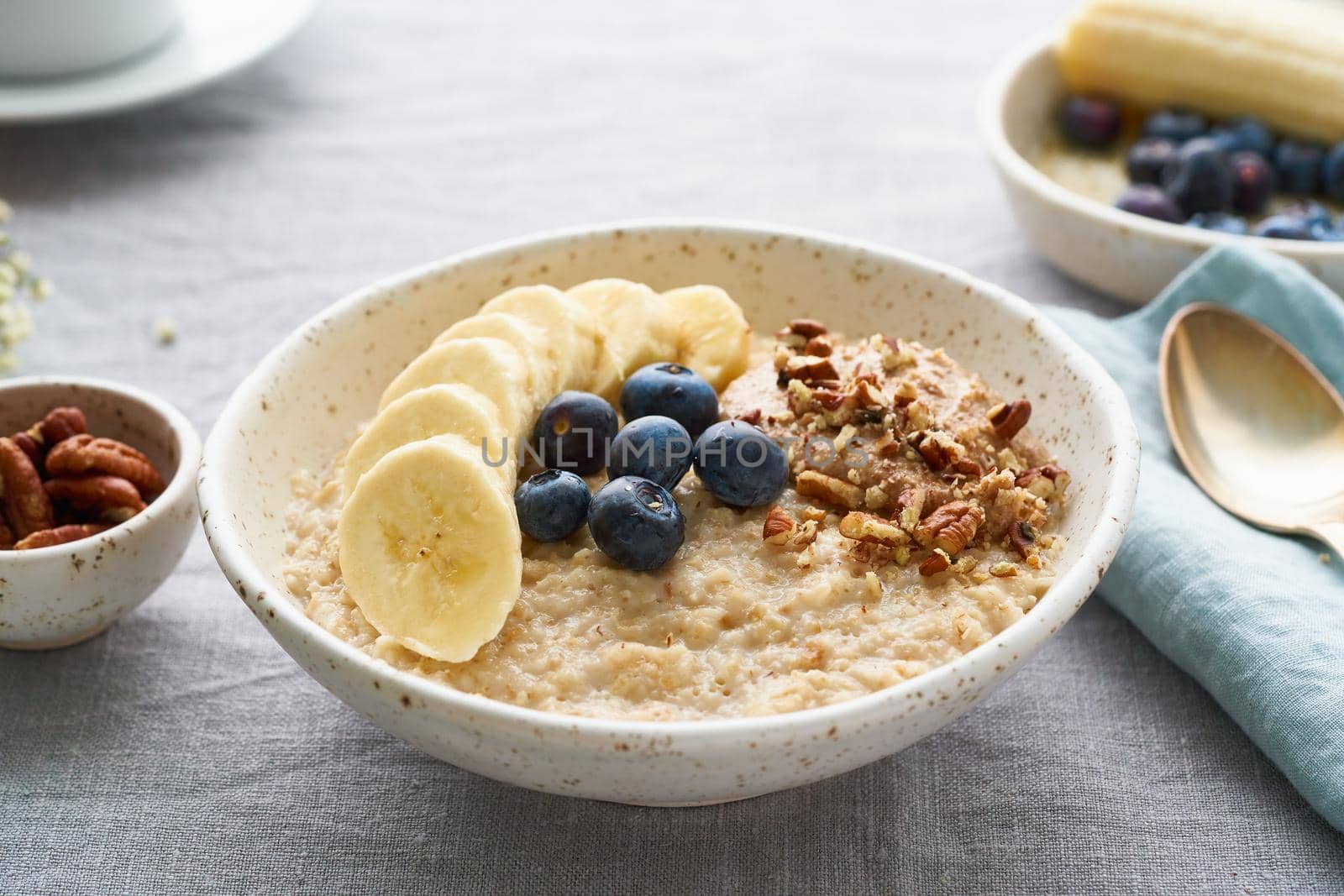 Whole oatmeal, large bowl of porridge with banana, blueberries, nuts for breakfast, by NataBene