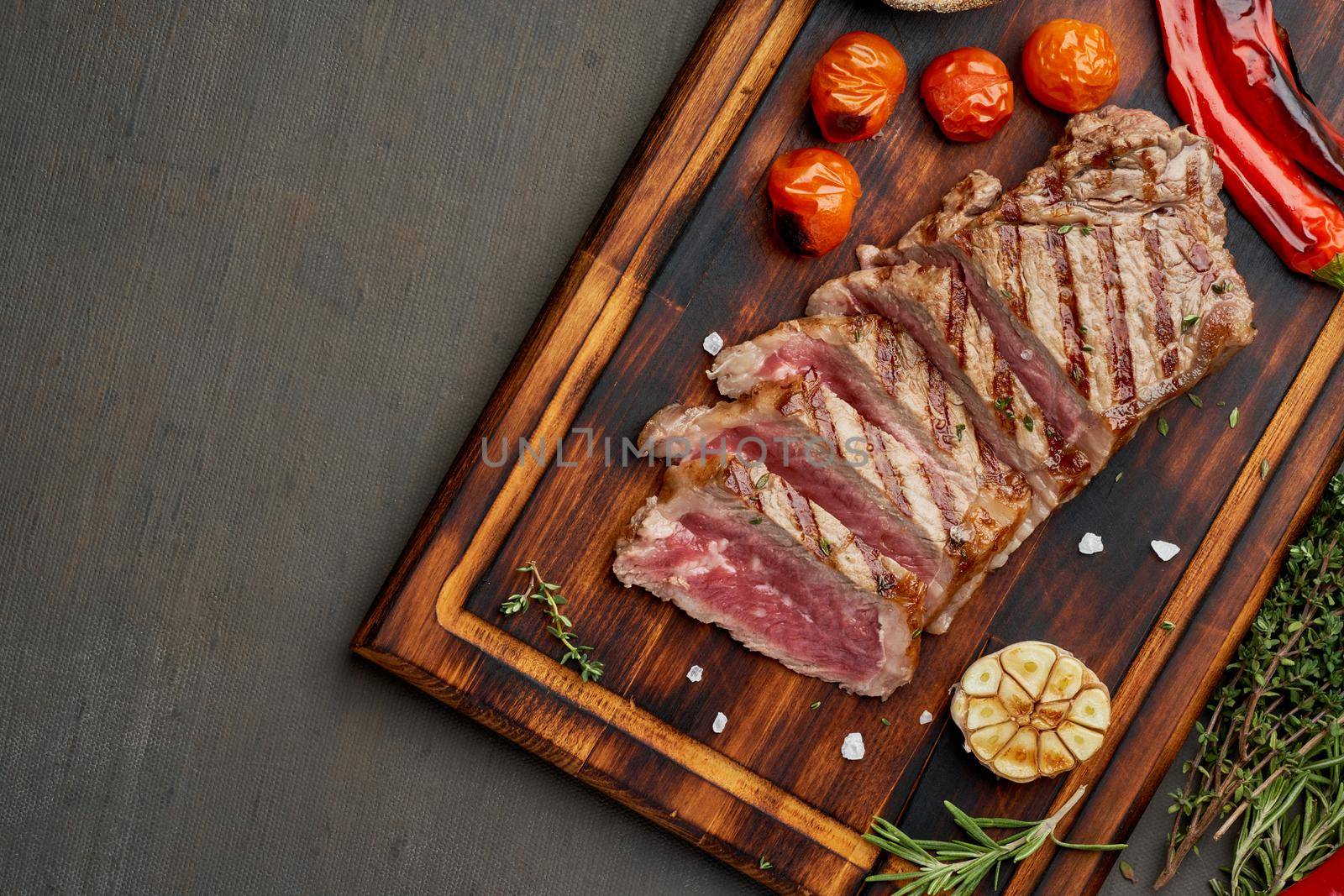 Keto ketogenic diet grilled fried beef steak, striploin on cutting board on dark brown table. Paleo food recipe with grilled fried chopped piece of meat, papper, top view, copy space