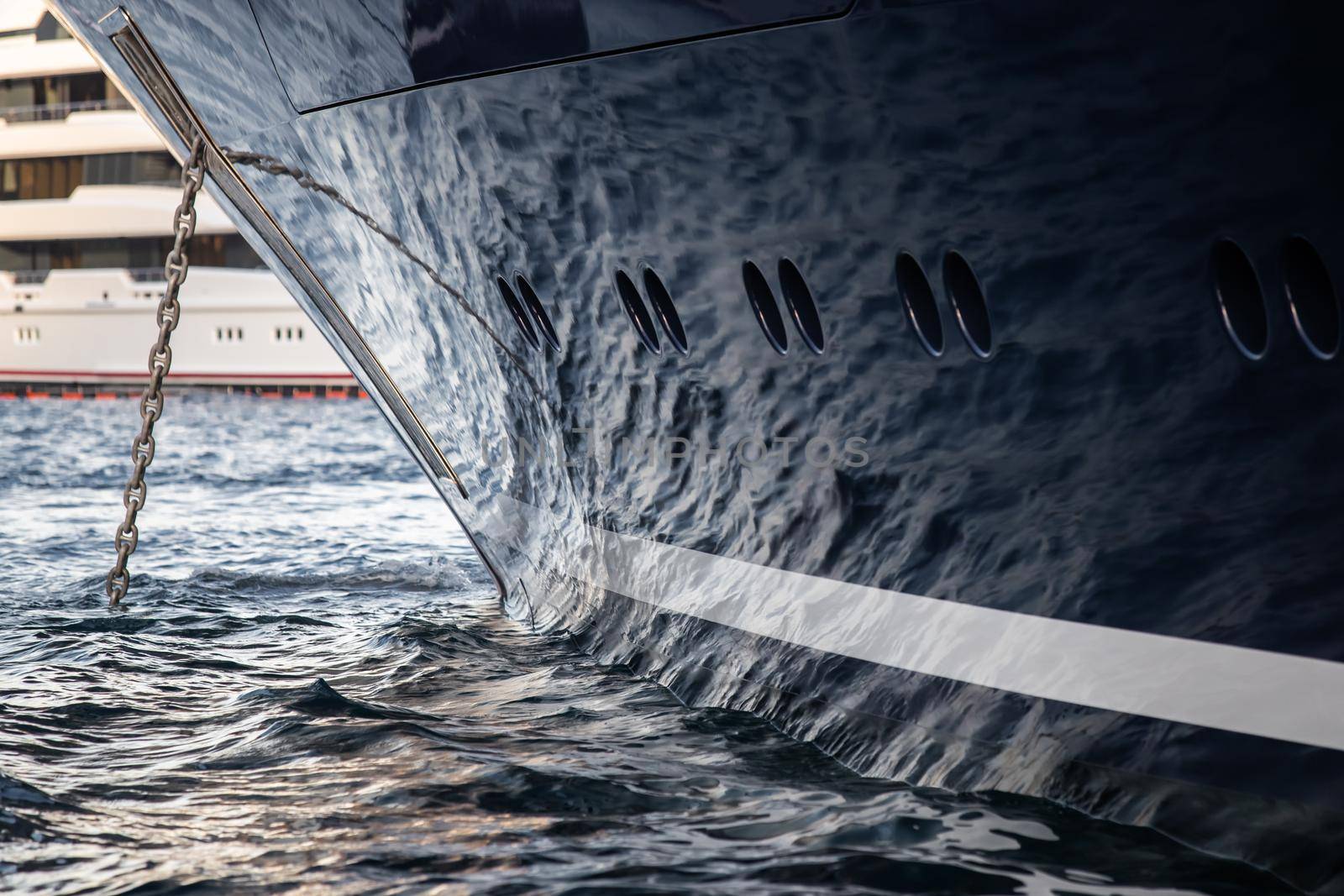 The mesmerizing reflection of the water on the glossy side of a huge yacht anchored, chrome details, chains and ropes to the muring descend into the water. High quality photo