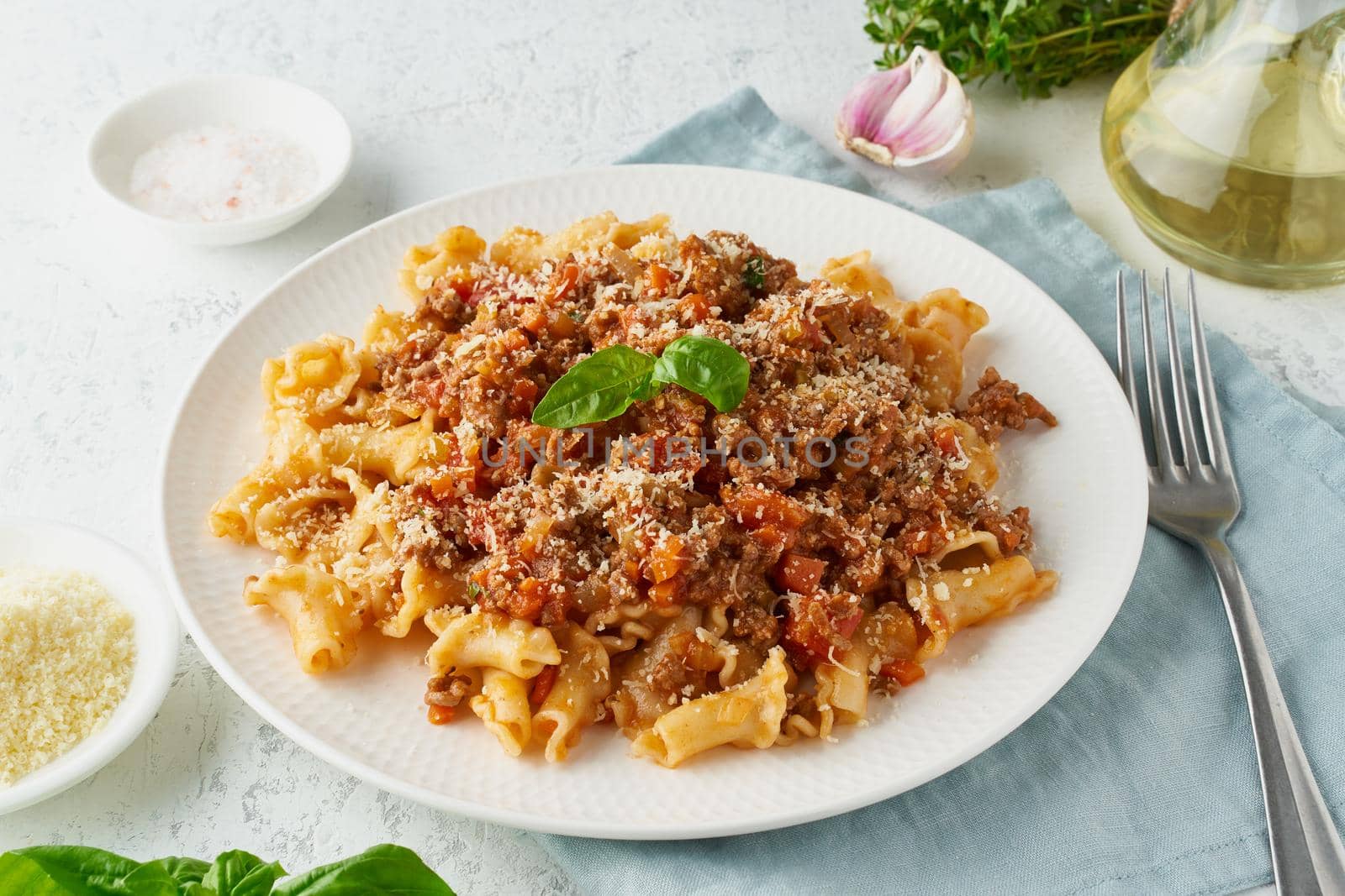 Pasta Bolognese campanelle with mincemeat and tomato sauce, parmesan cheese, basil. Italian dinner, white table. , side view, close up