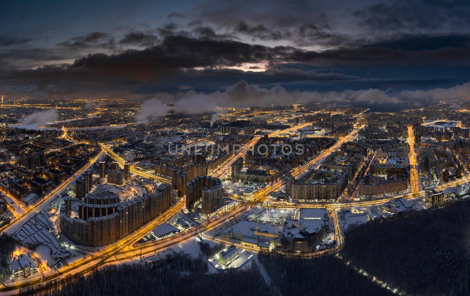 Aerial winter cityscape of St. Petersburg - Russia at dusk, drone flies over huge housing estates and public park, construction cranes, night illumination, clouds float below drone. High quality photo
