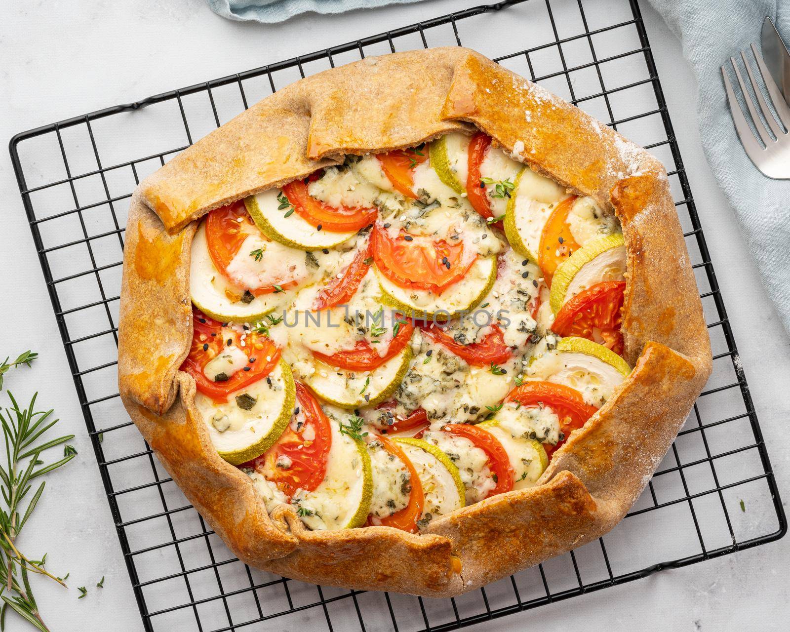 Homemade savory galette with vegetables, wholegrain pie with tomatoes, zucchini, blue cheese Gorgonzola. Rustic crust crostata on dark linen textile tablecloth. Top view