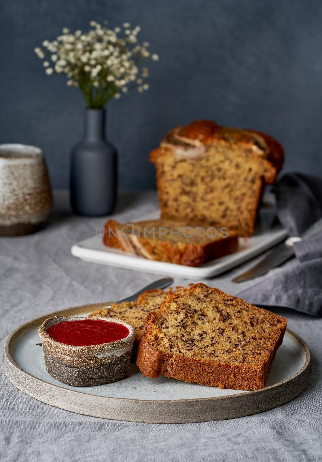 Banana bread. Cake with banana, traditional american cuisine. Slices of loaf with raspberry jam. Dark background, black table, shadows. Side view, close up.