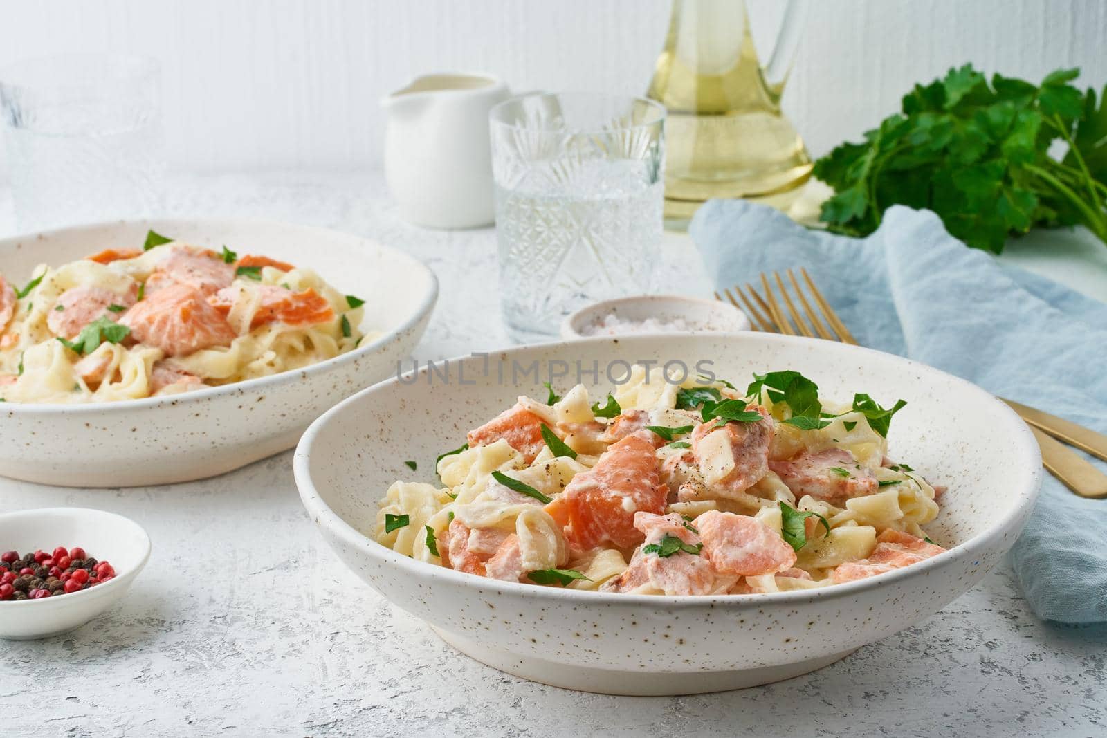 Salmon pasta, tagliatelle with fish and creamy sauce. Italian dinner with seafood for two at table. White background, side view