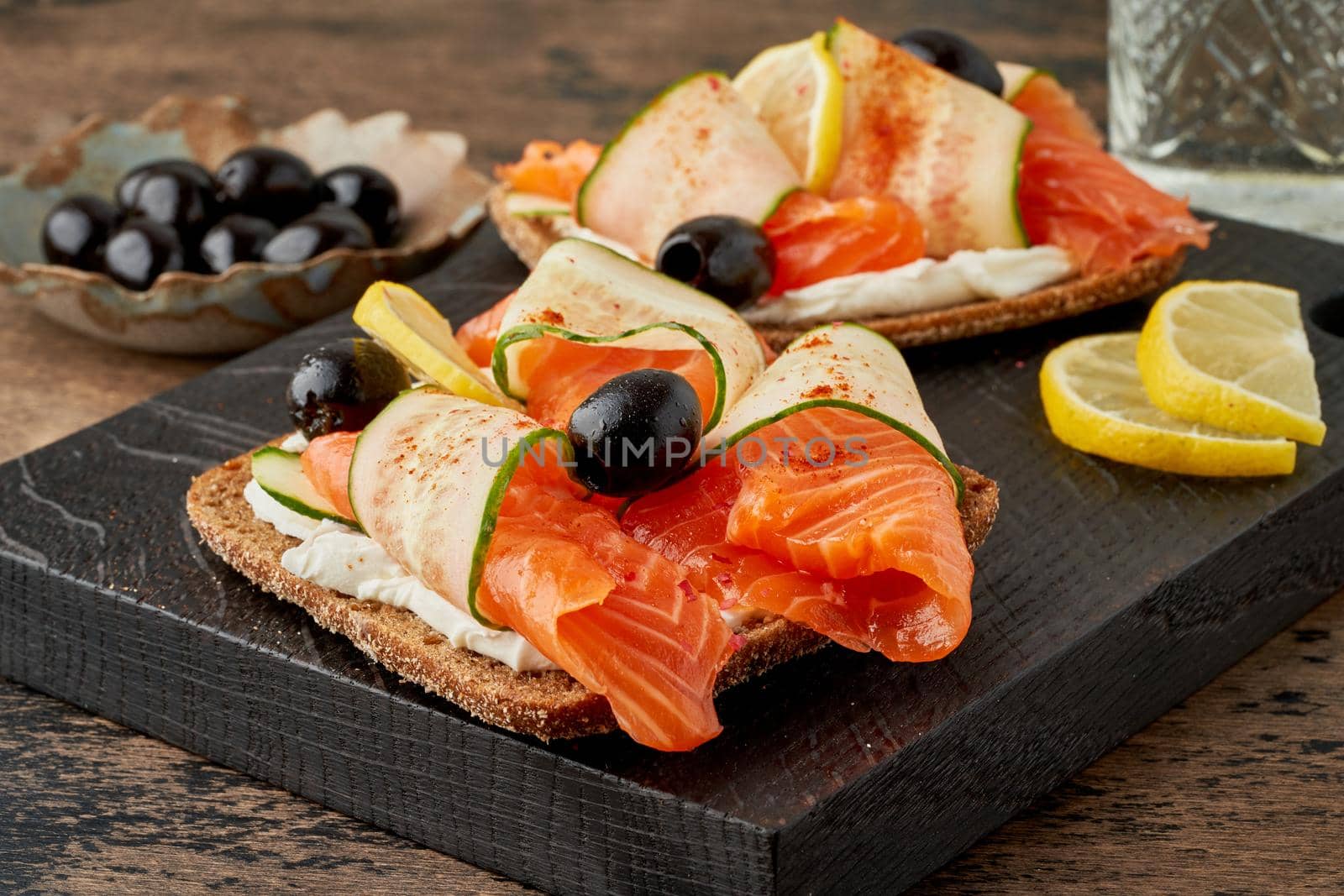 Smorrebrod - traditional Danish sandwiches. Black rye bread with salmon, cream cheese, cucumber and olives on dark brown wooden background