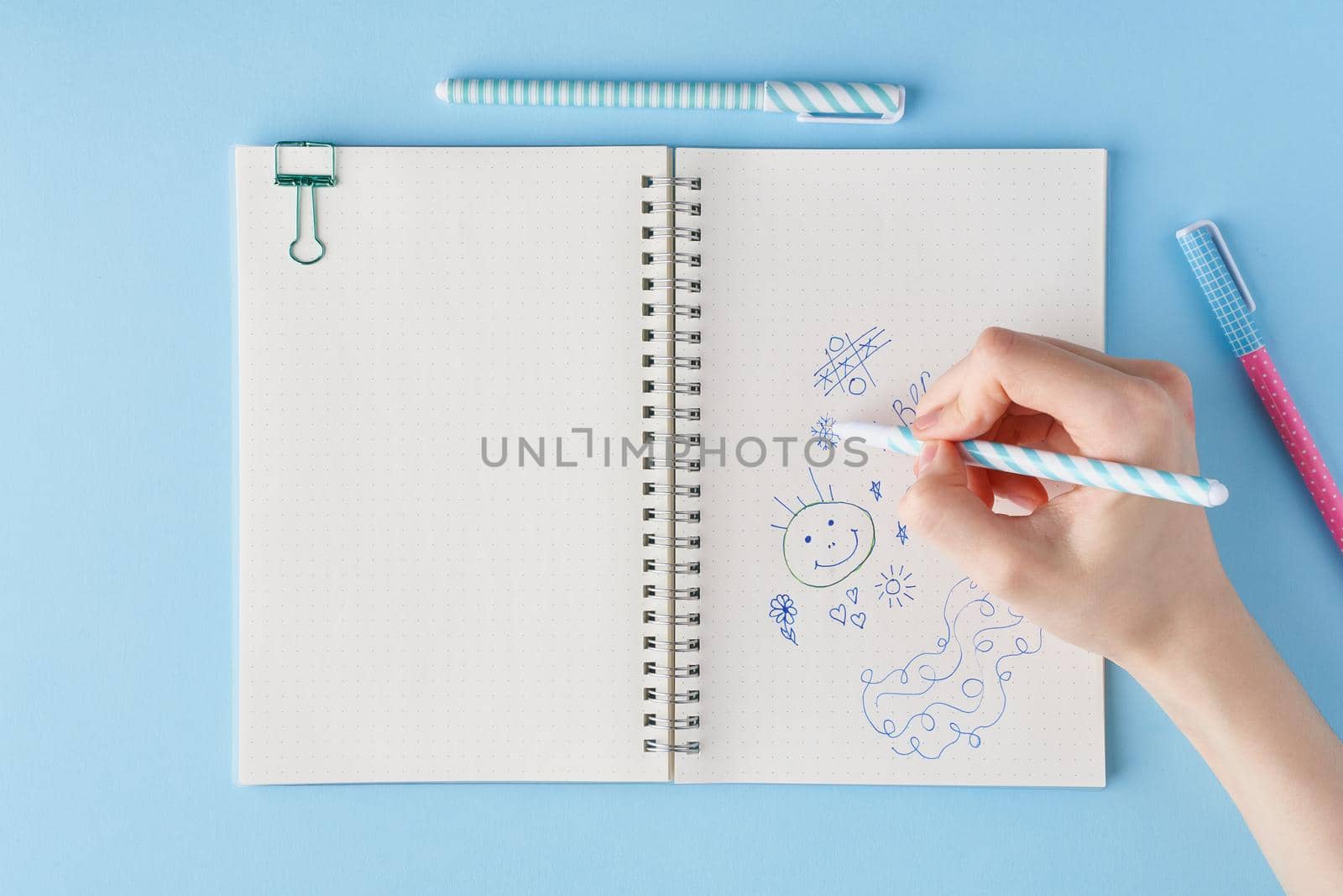 Hand draws scribble in a notebook. Blank notepad page in bullet journal on bright blue office desktop. Top view of modern table with notebook, stationery. Mock up, copy space