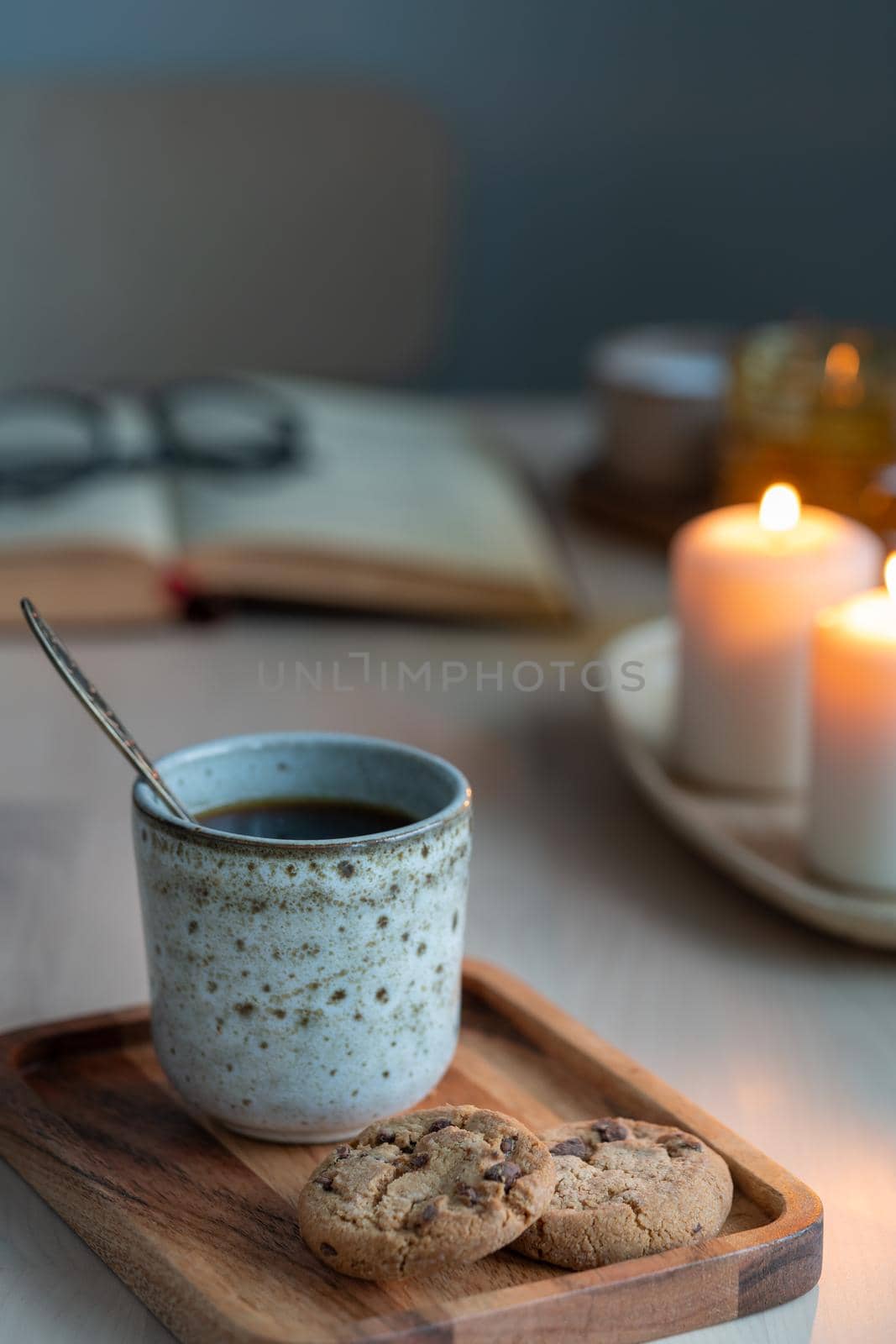 Cozy background with book, chocolate chip cookies, cup of tea. Sunday evening, mug of drink, holiday decorations, candles lights bokeh. Vertical still life twilight